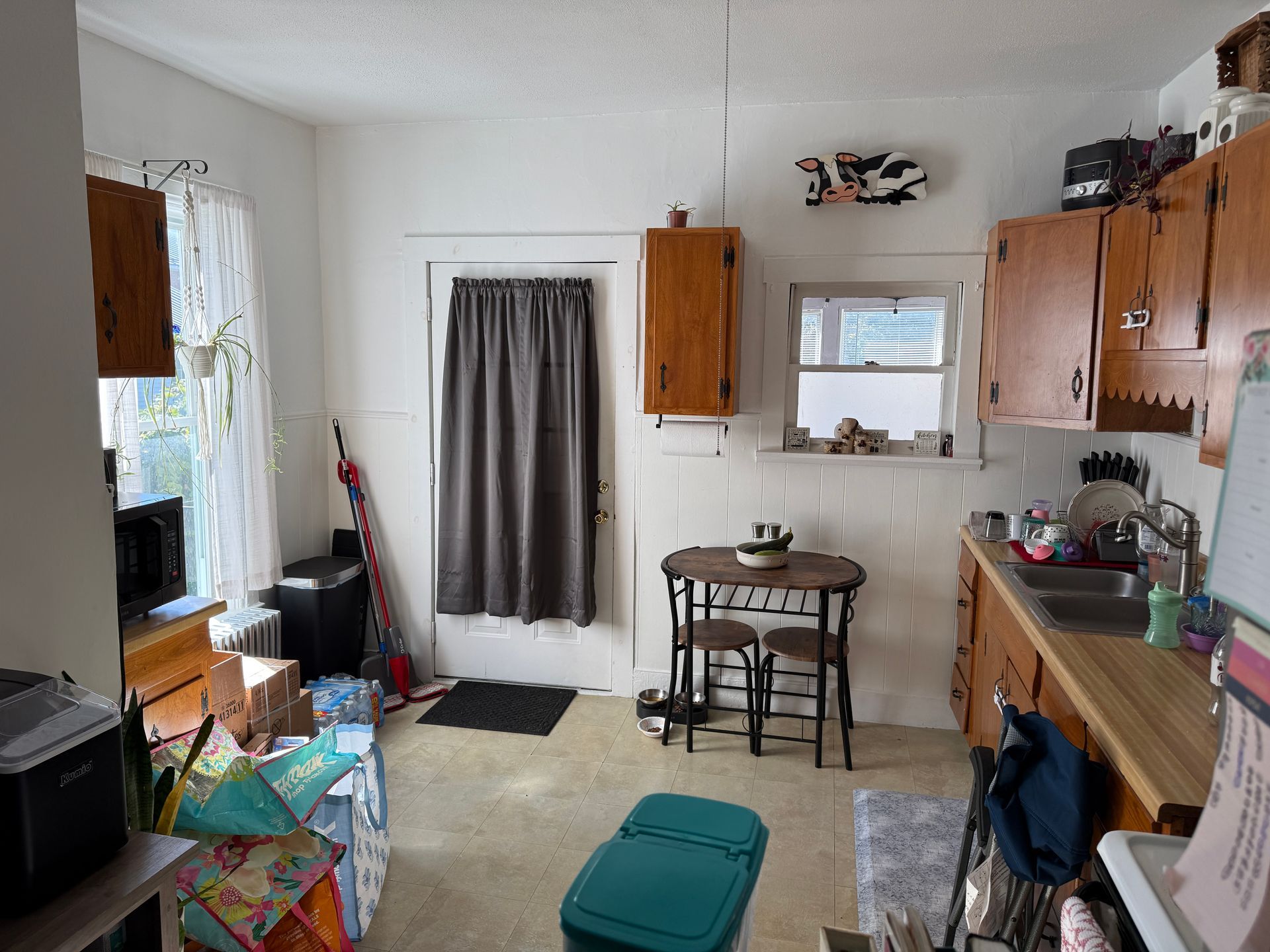 Small kitchen with cabinets, sink, round table, and various items.