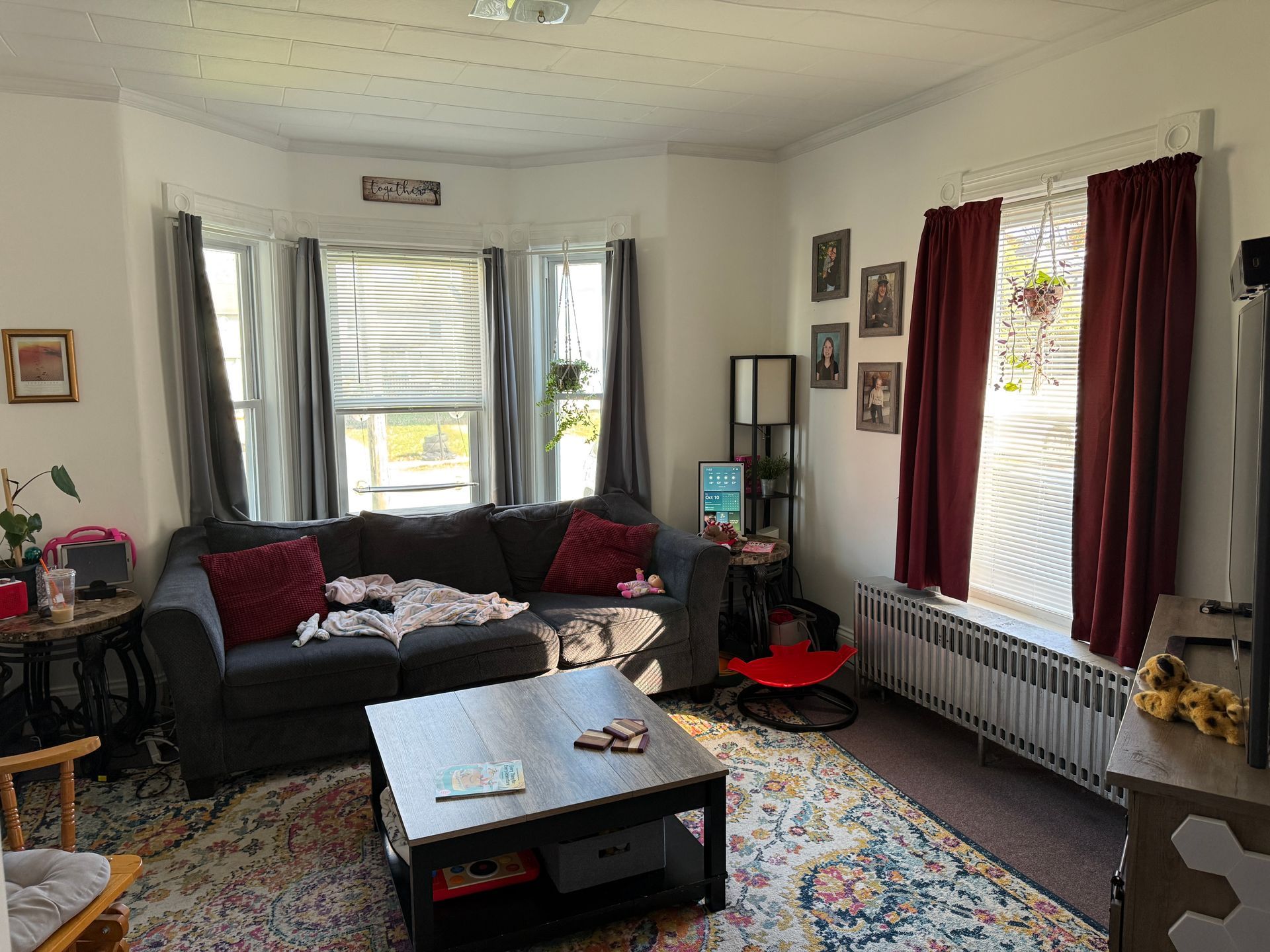 Living room with gray sectional, coffee table, rug, windows, and red curtains.