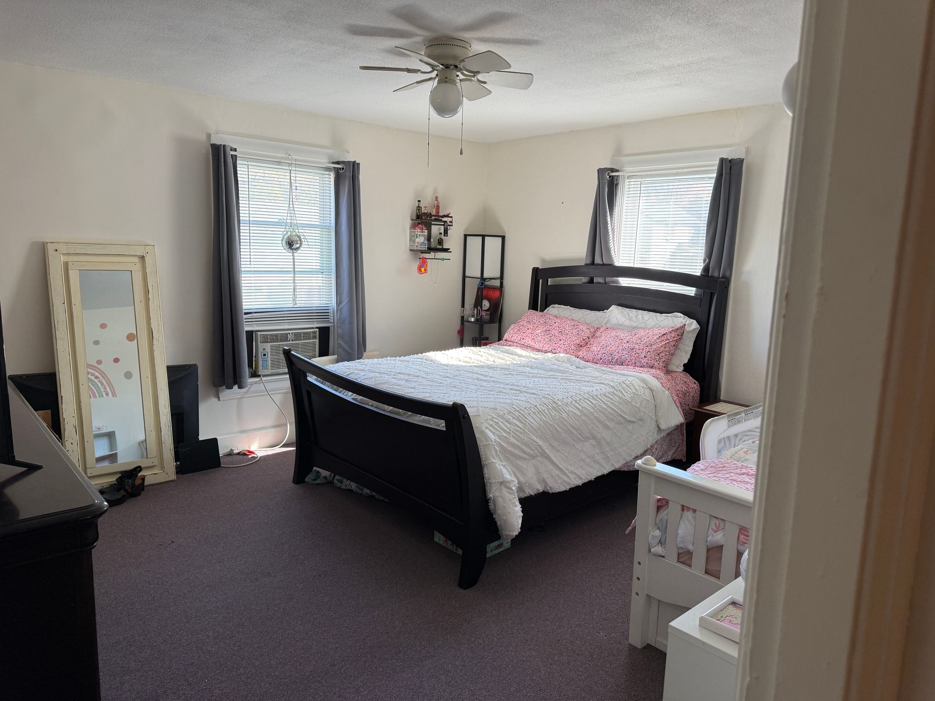 Bedroom with a bed, dresser, mirror, windows, and a small crib.