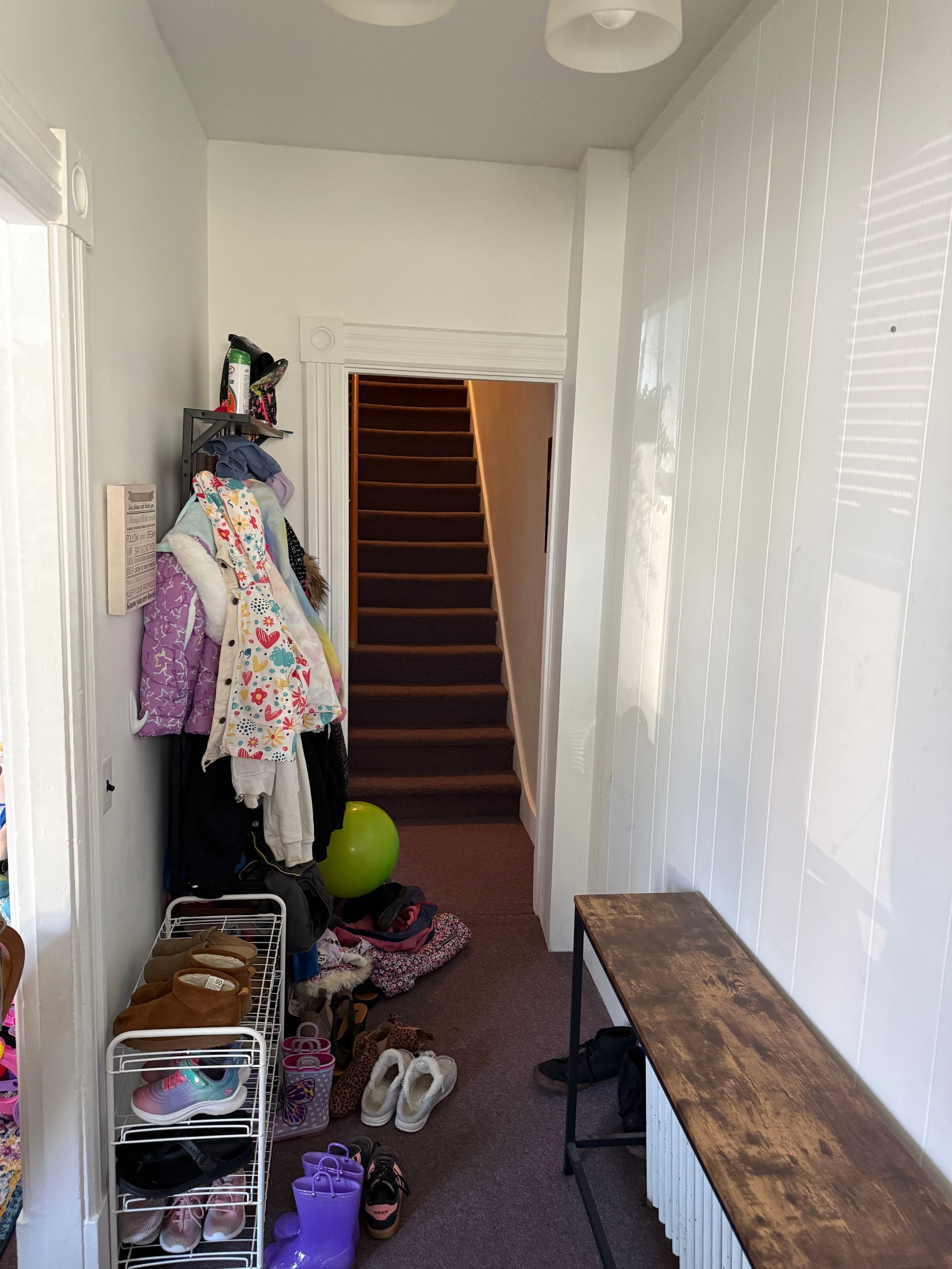 Hallway with staircase, shoe rack, clothes rack, bench, and items.