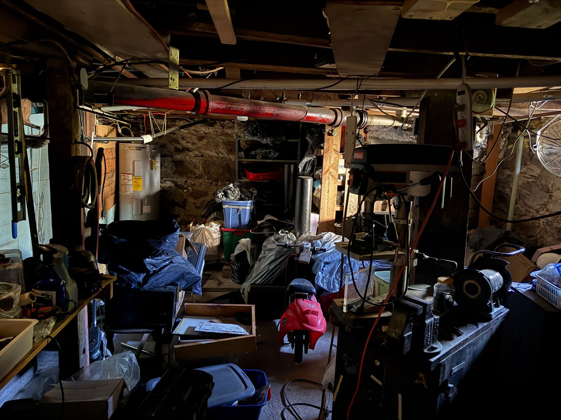 Basement workshop with exposed pipes, tools, and storage.