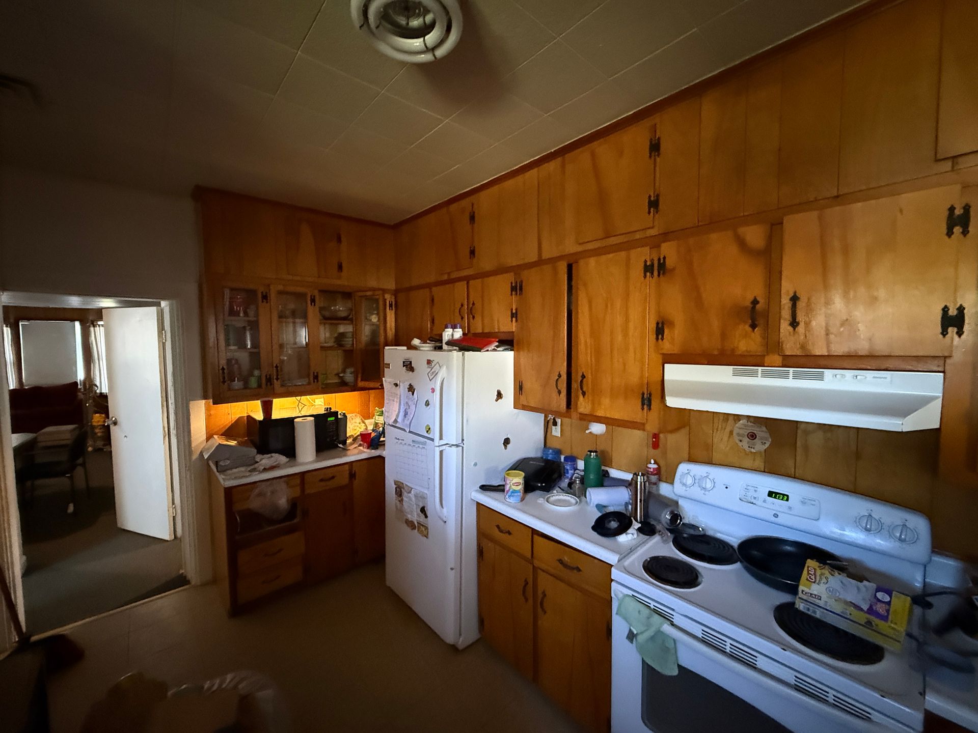 Kitchen with wood cabinets, white appliances, and a stove. Open door leads to a room with a red armchair.