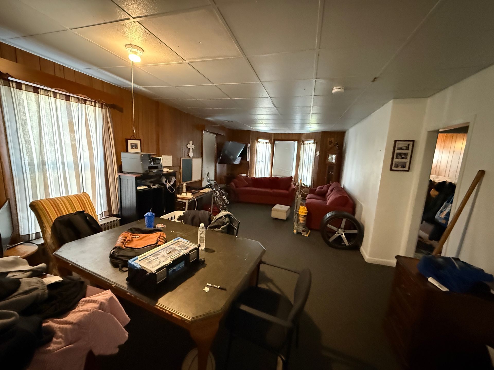 Spacious living room with a dining table, red sofa, and electronics against wood-paneled walls.