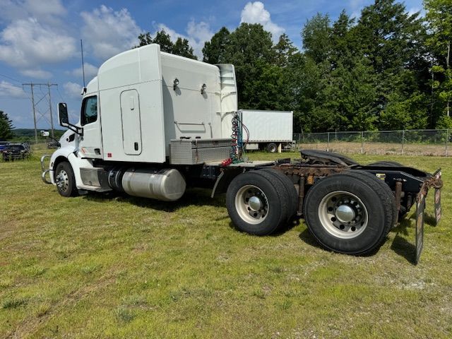White semi-truck parked on grassy field, with trees and cloudy sky in the background.