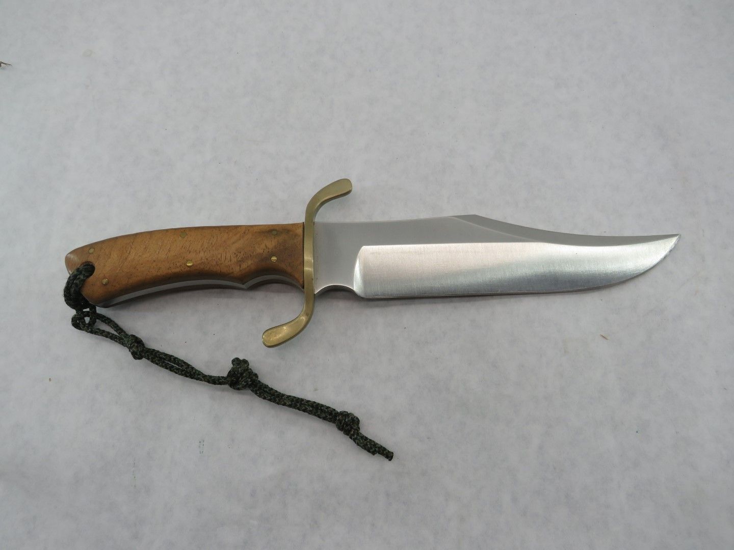 Bowie knife with wooden handle, brass guard, and shiny blade lying on a light surface.