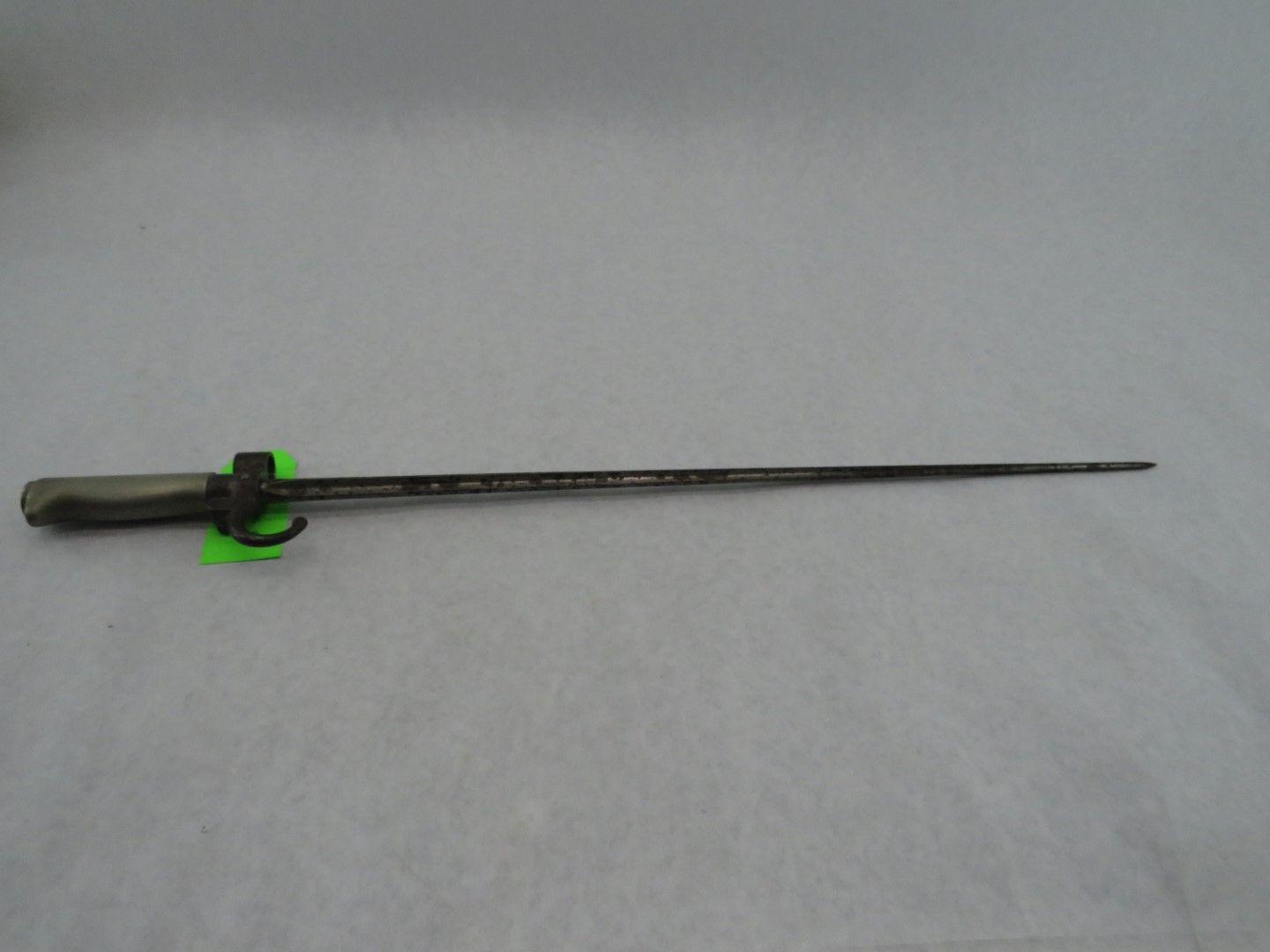 Bayonet, dark metal blade with a handle, mounted with a green tag.