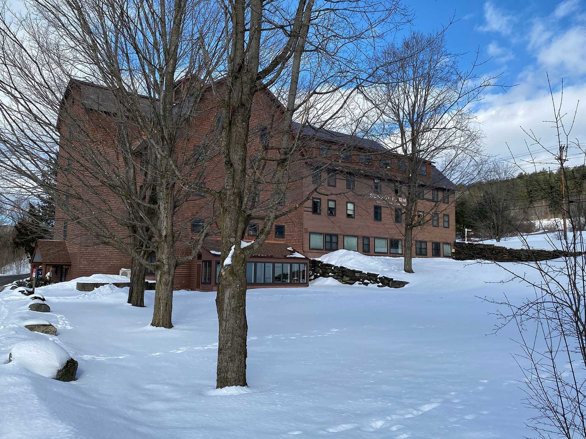 A large brick building in a snowy landscape, trees in front, under a blue sky.