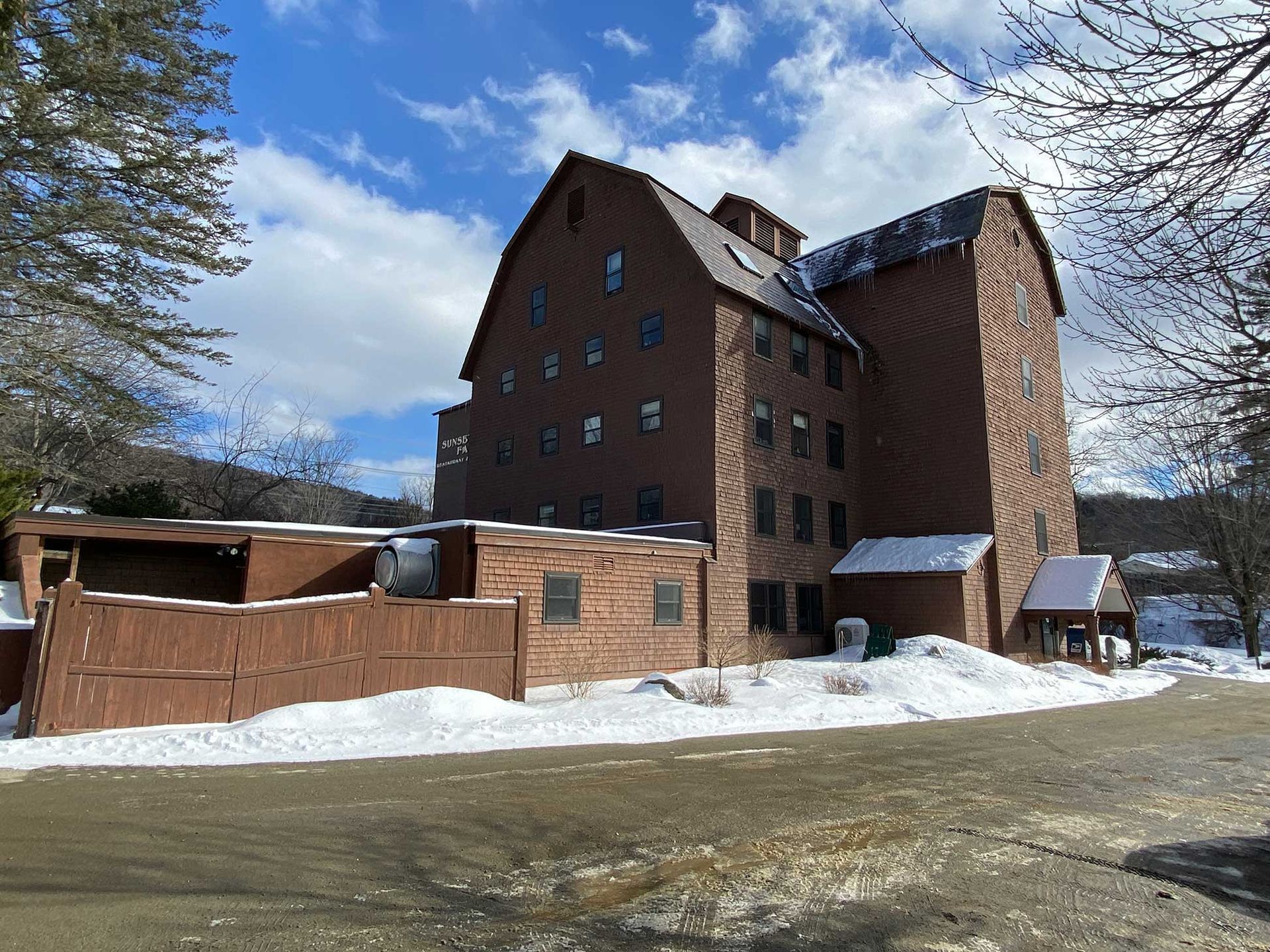 Brick building with snow, cloudy sky, brown fence.
