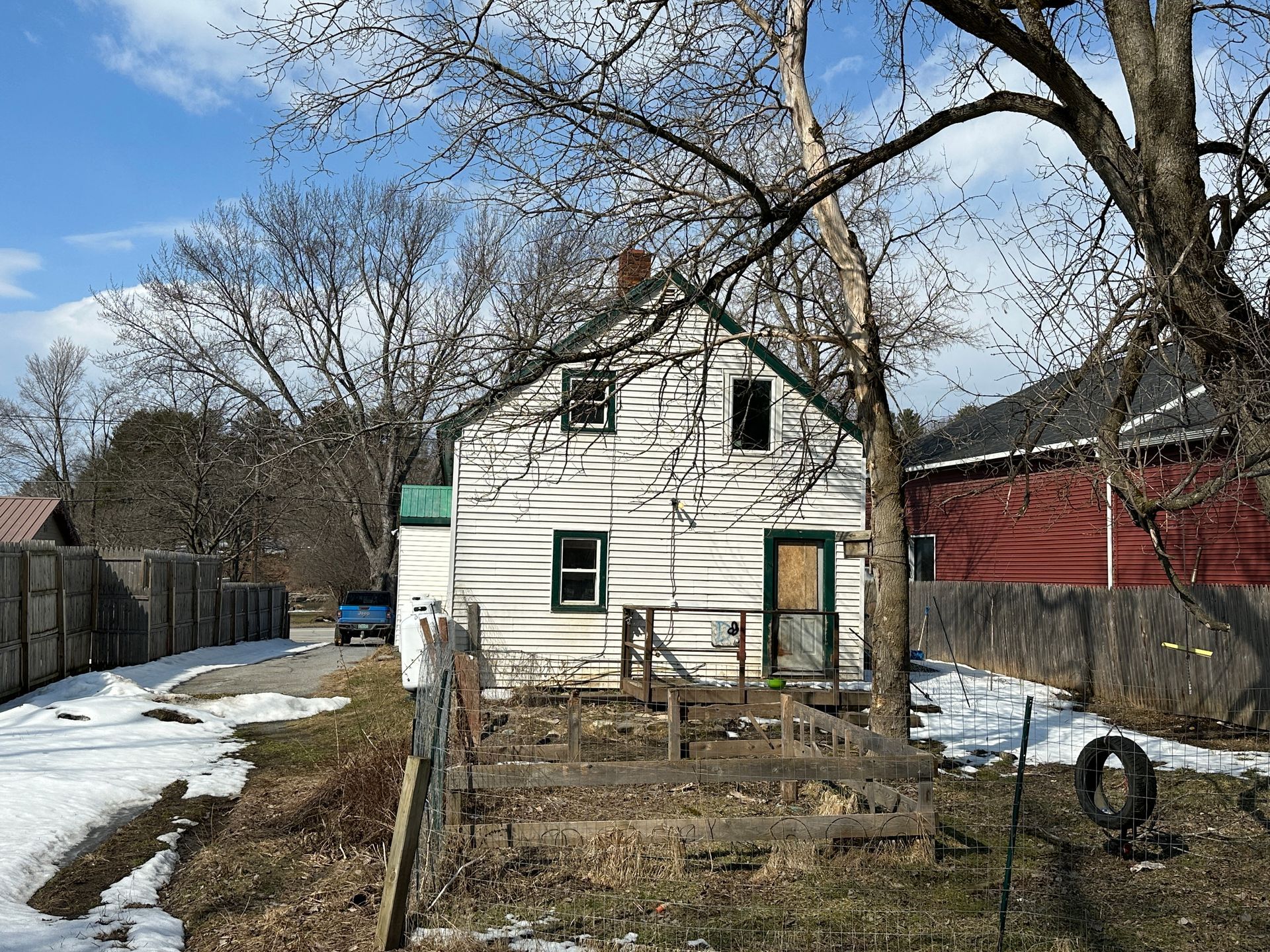 A white, two-story house with a fenced garden area in front, situated on a snowy lot.