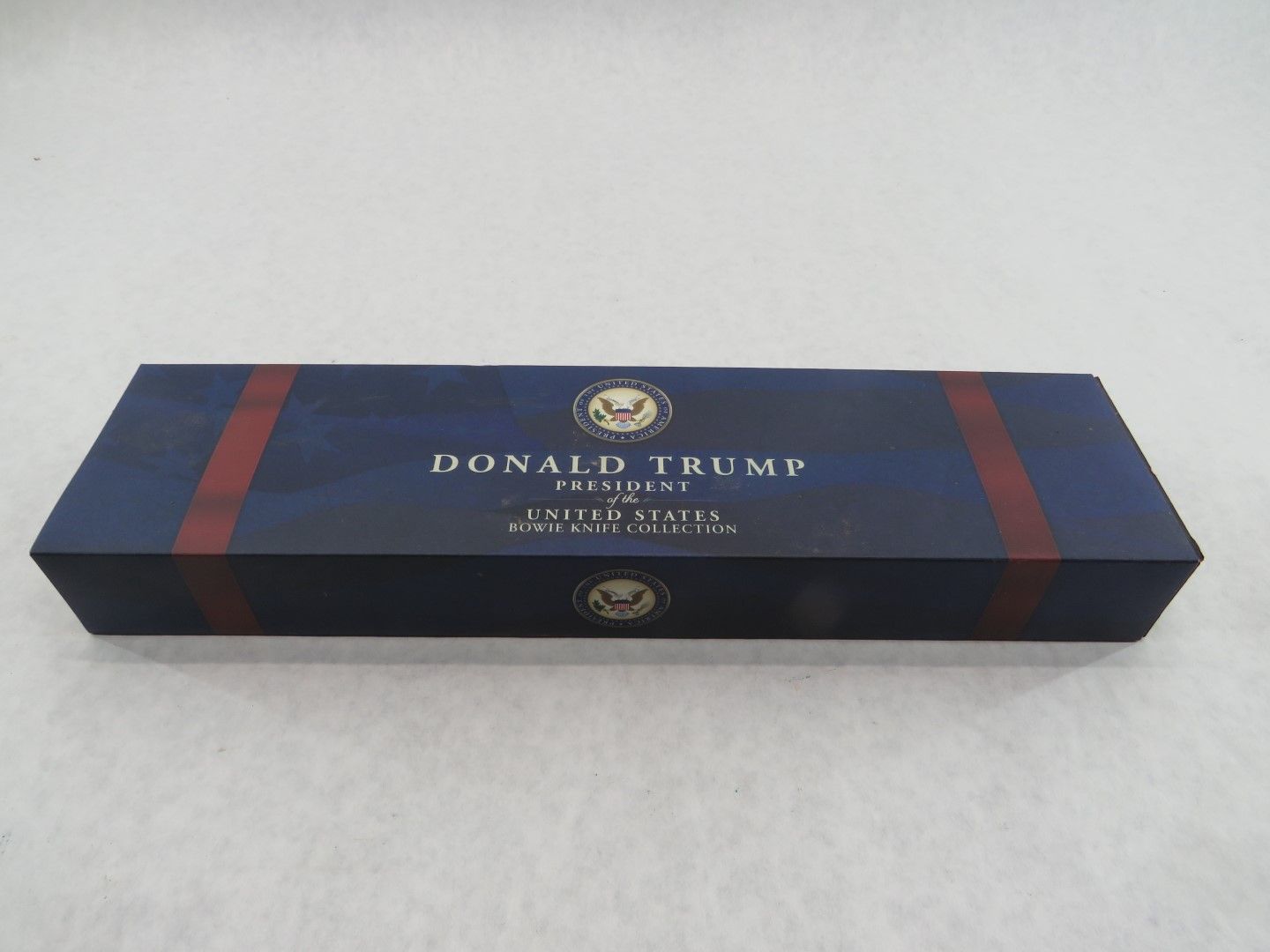 Navy blue box with text and presidential seal. Red stripes adorn the sides.