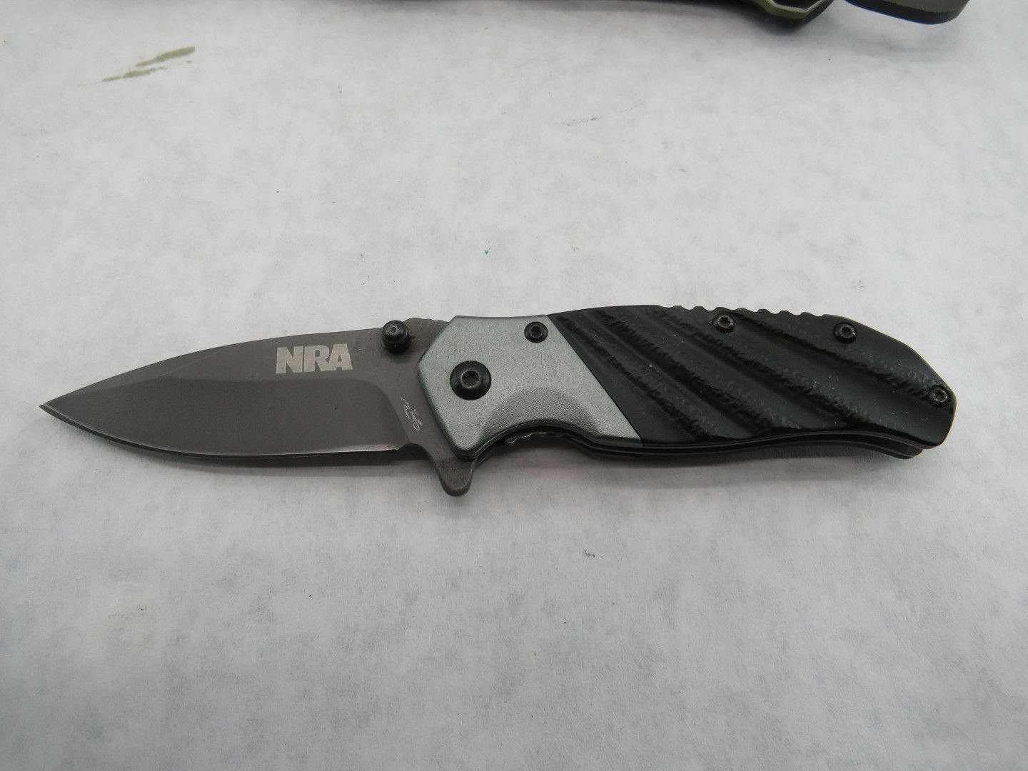 Black NRA folding knife with gray accents on a white surface.