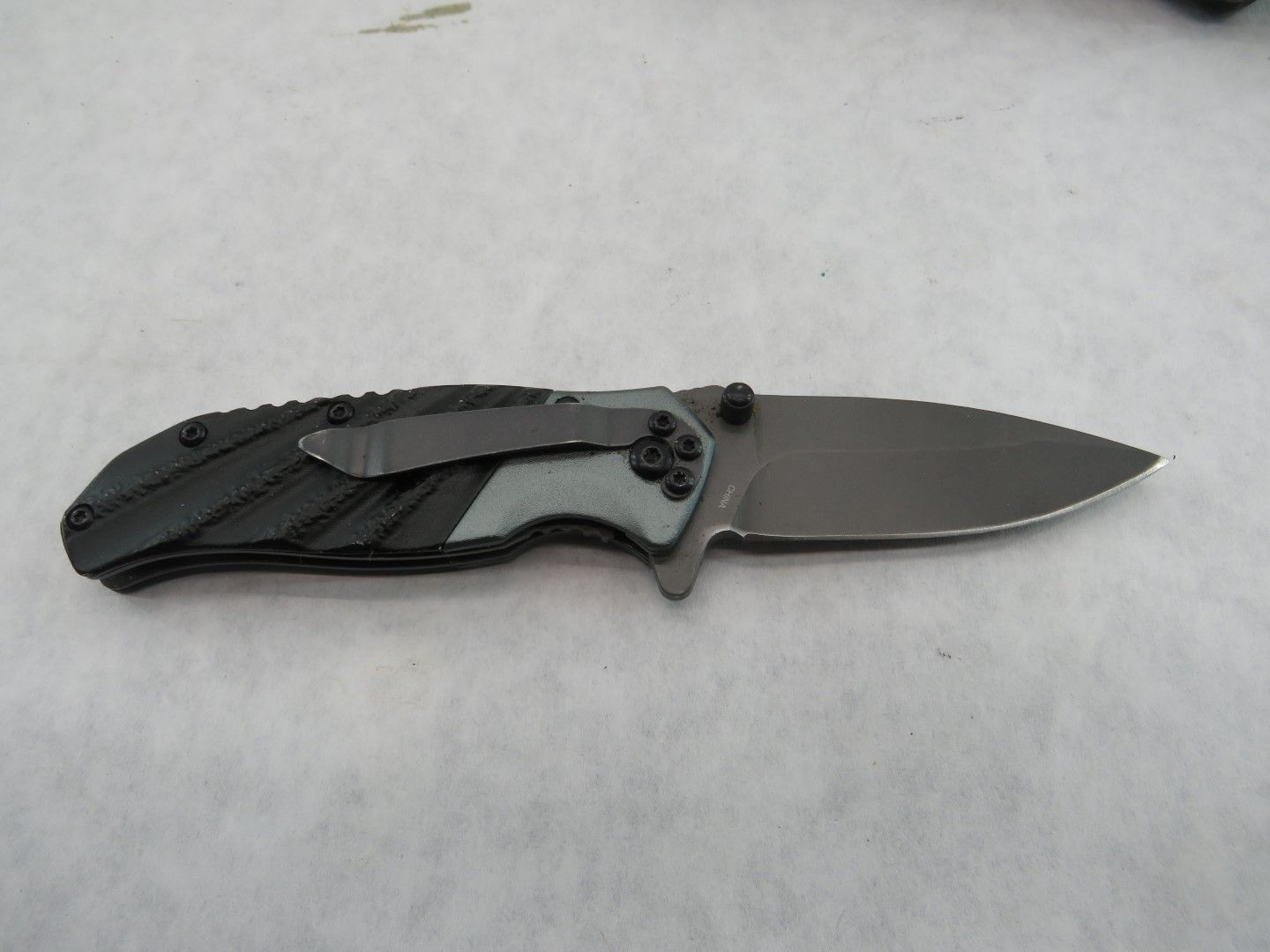 Black folding knife with a partially open blade, pocket clip, and gray handle details.