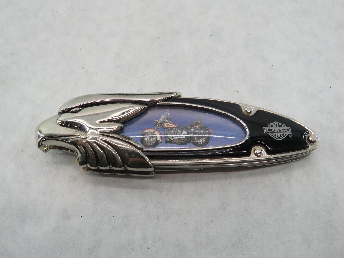Silver and black Harley Davidson pocket knife with eagle head design, small motorcycle inside.