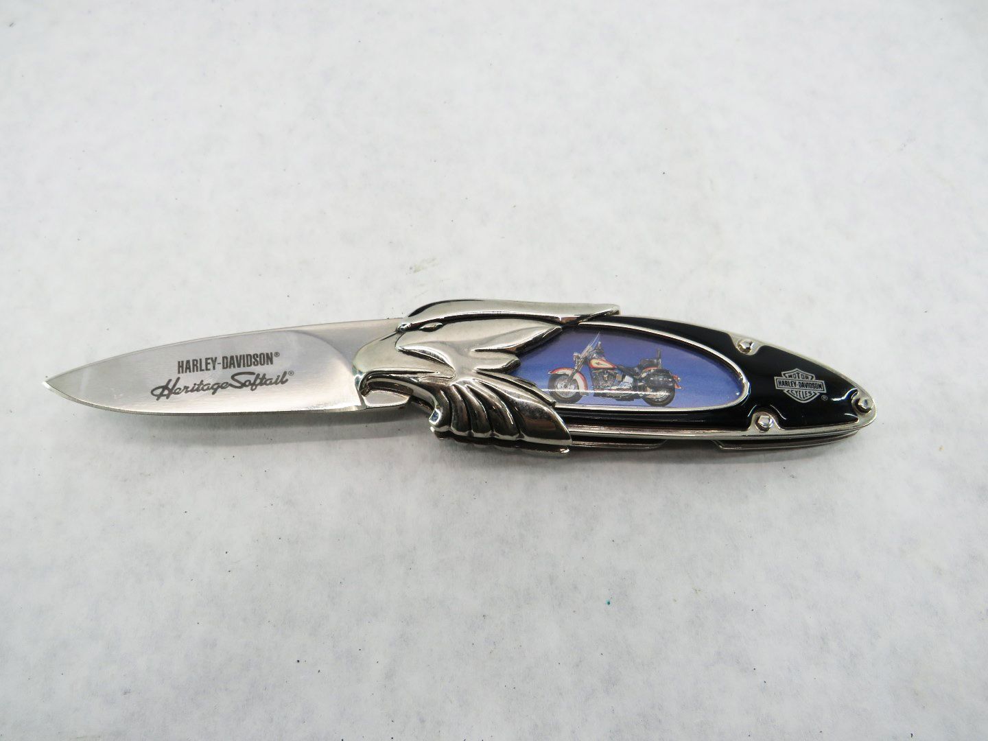 Harley-Davidson pocket knife with motorcycle design, chrome handle, and blue inlay on a white surface.