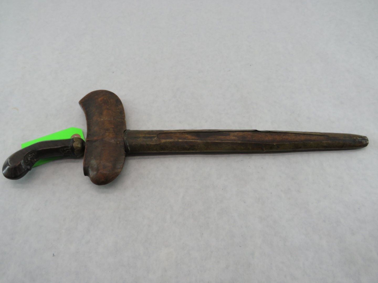 Wooden keris dagger with curved hilt and wavy blade, resting on a light grey surface.