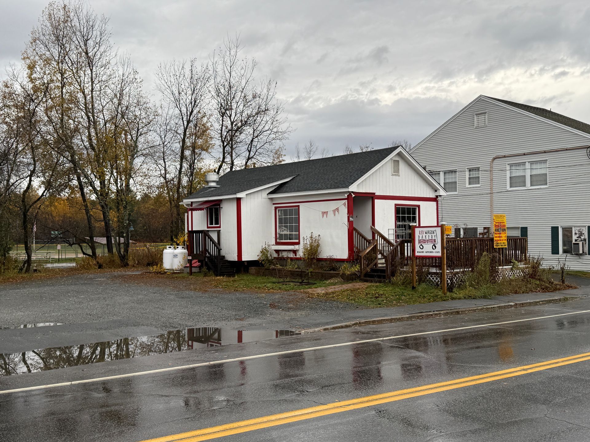 Small white building with red trim, next to a larger gray building on a cloudy day.
