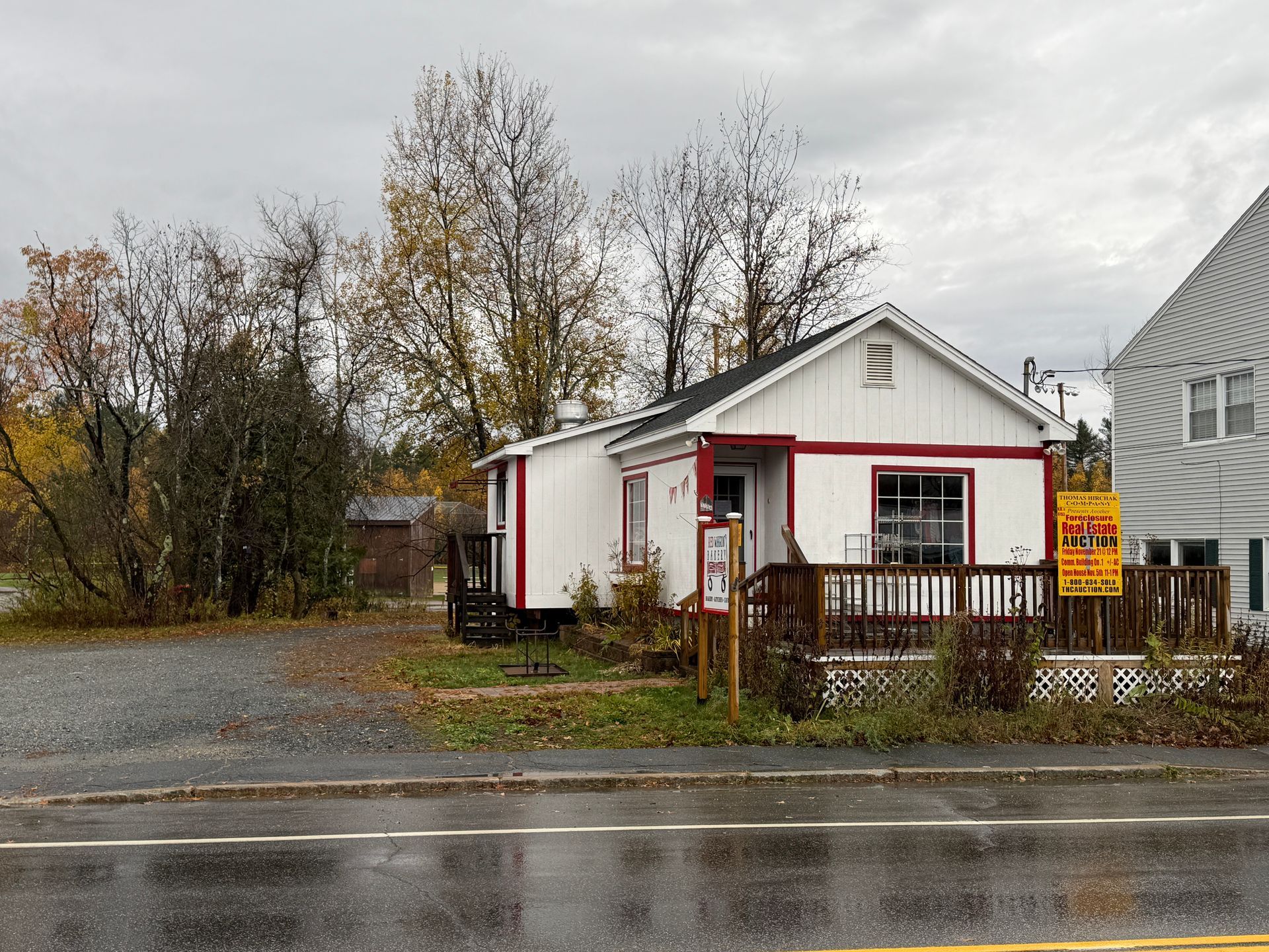 White building with red trim, small porch, sign on side, overcast day.