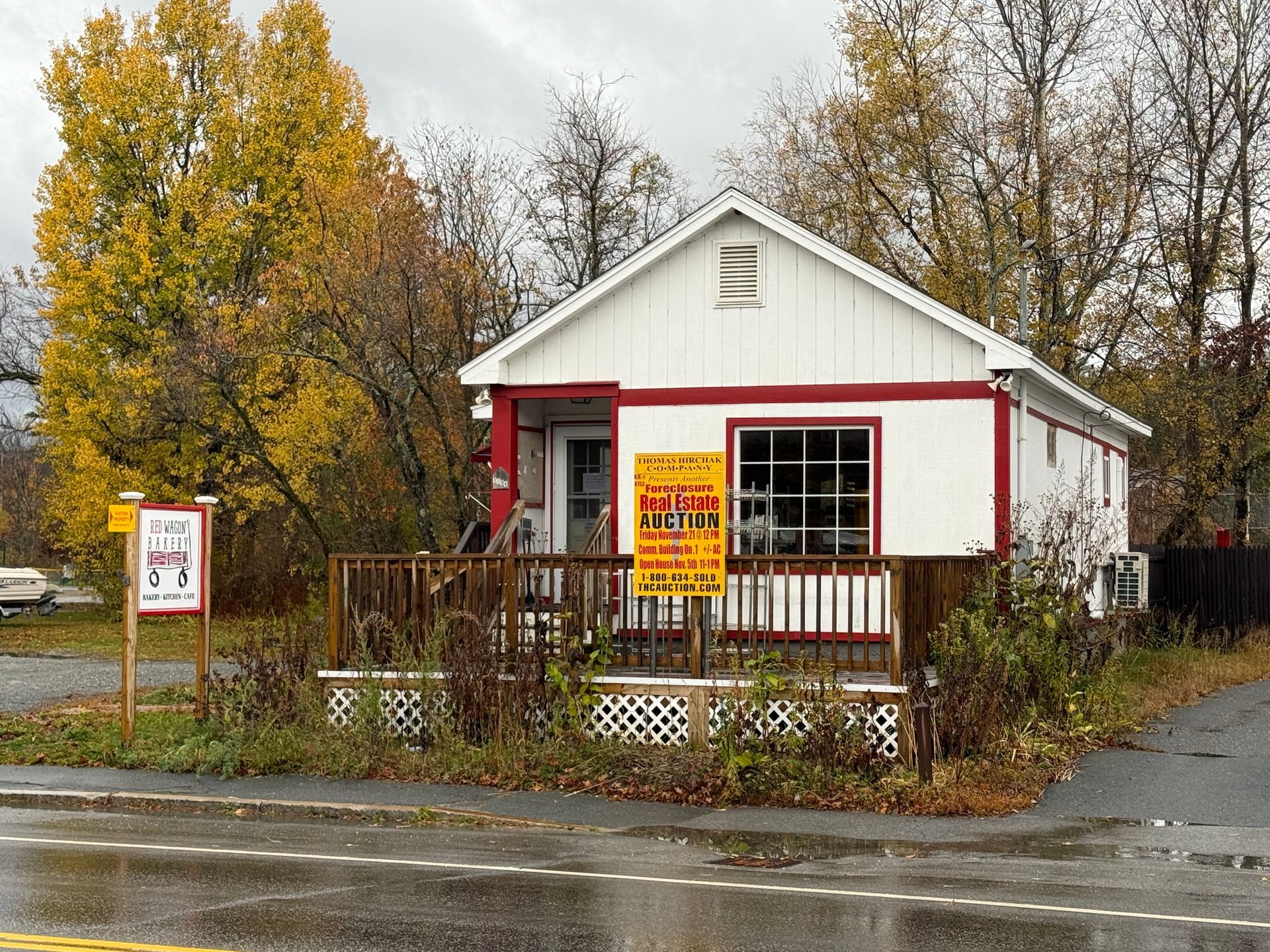 Small white building with red trim; a porch, signs, and fall foliage.