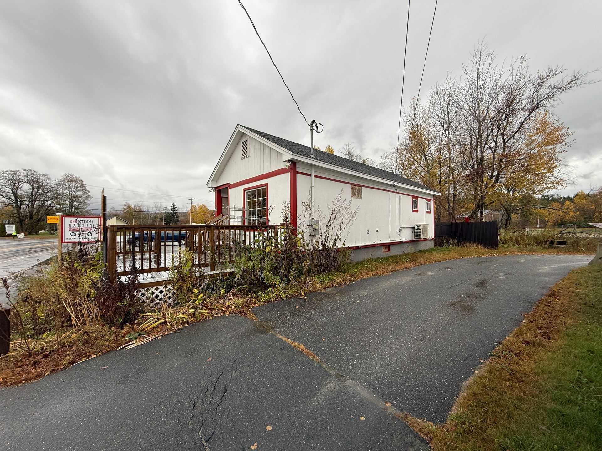 White building with red trim, deck, and driveway on a cloudy day.