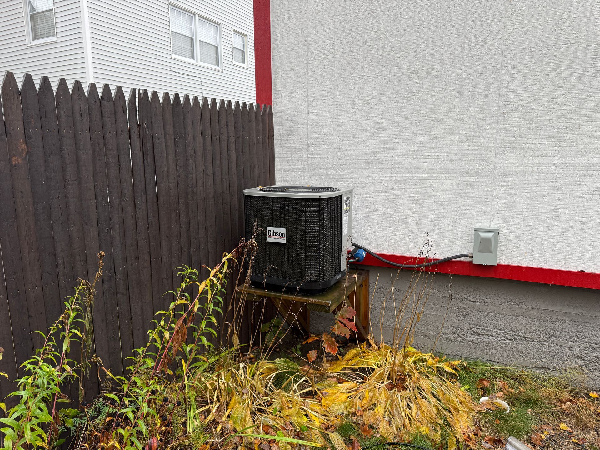 Air conditioning unit next to a brown wooden fence and white textured building.