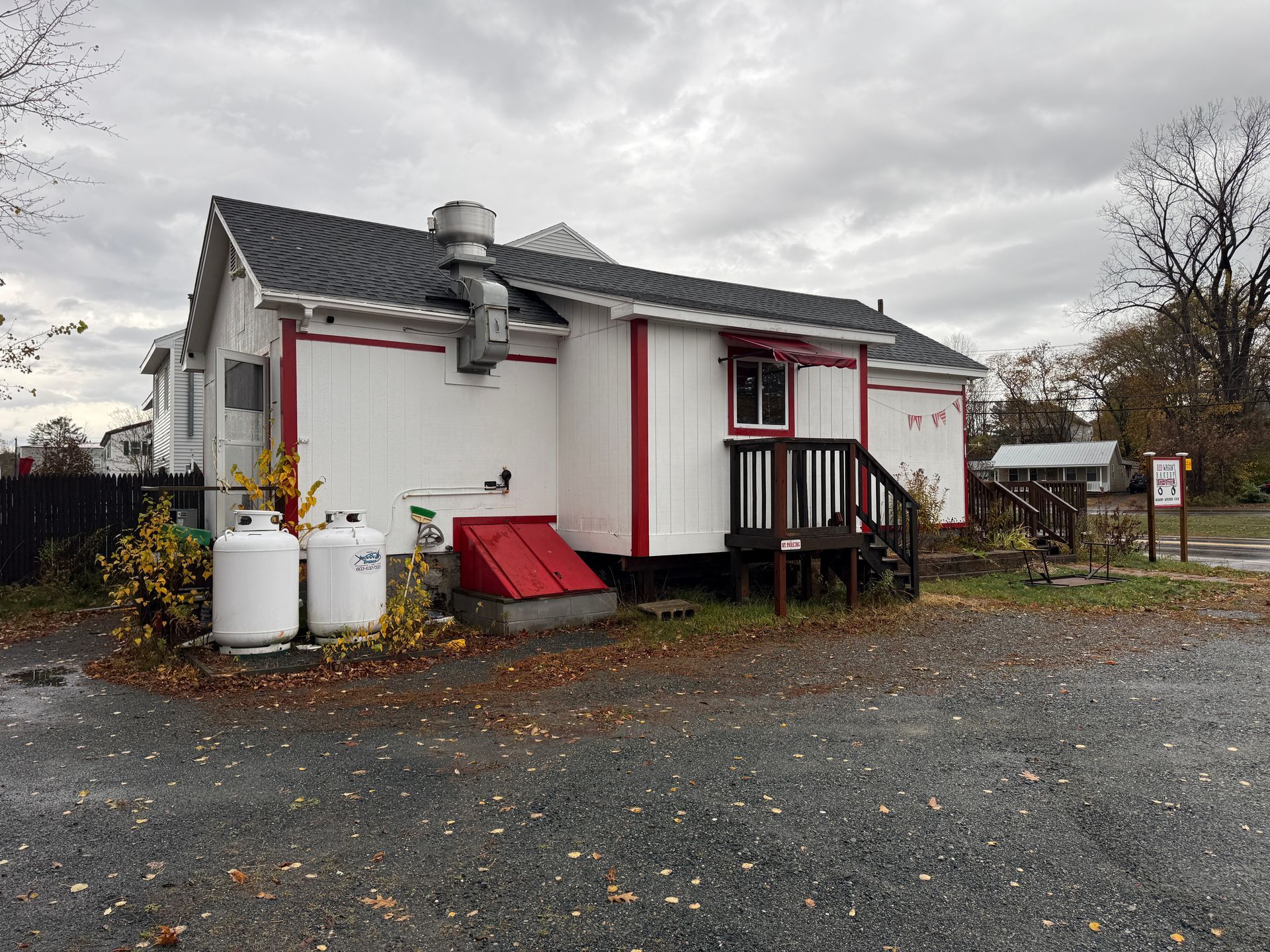 White building with red trim, chimney, and propane tanks. Overcast day.