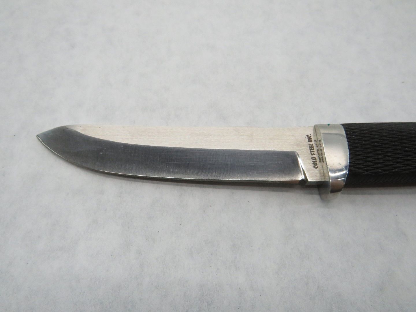 Close-up of a knife. The blade is silver, with a black textured handle.