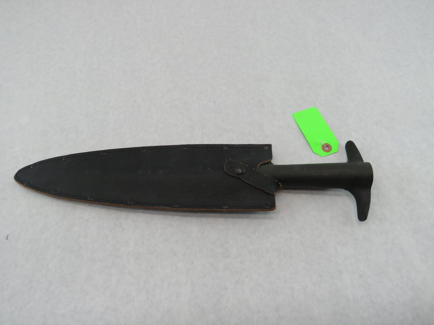 Black metal knife with a rounded blade and T-shaped handle, on a white surface.