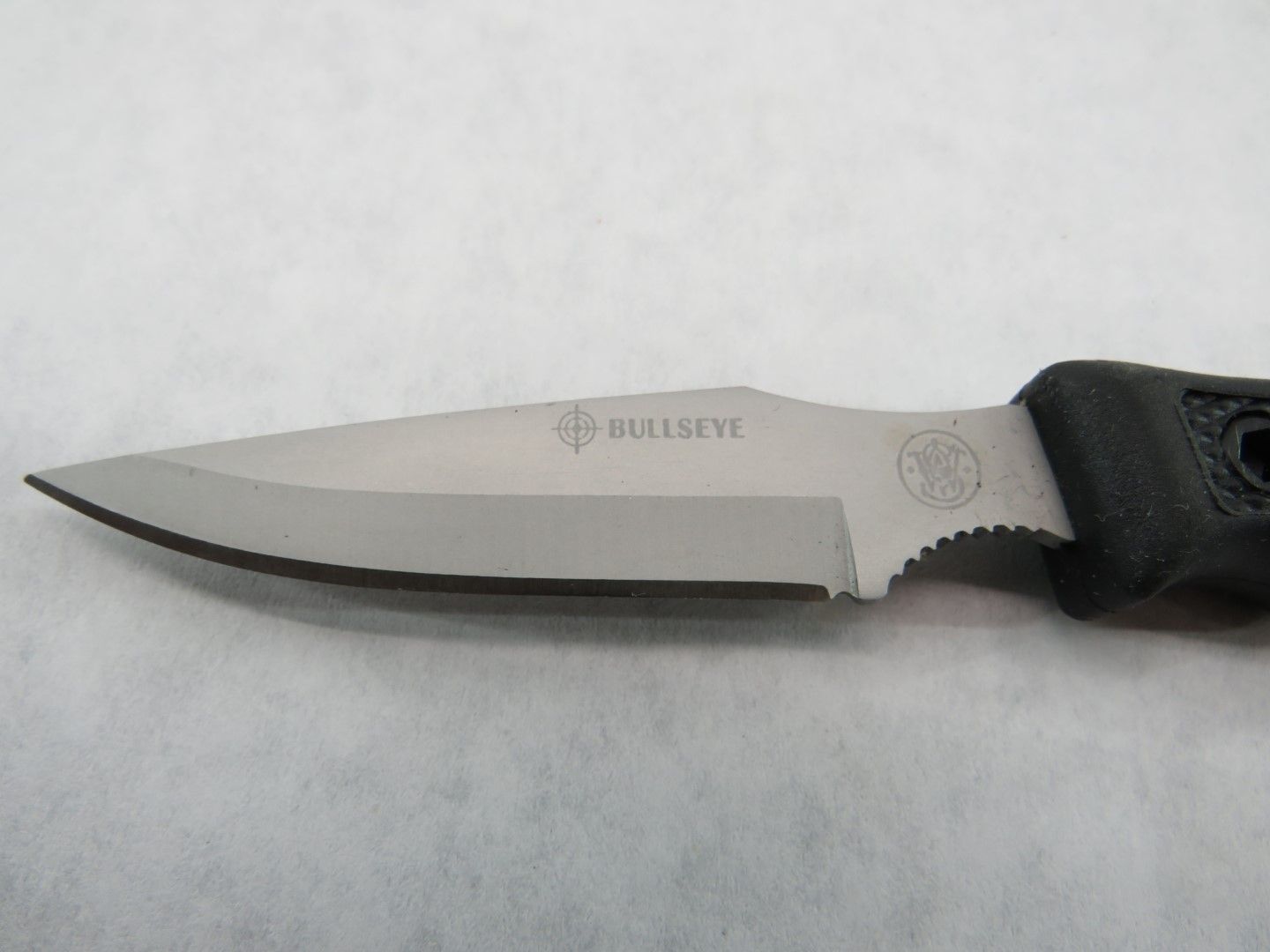 Close-up of a silver knife blade with a black handle, featuring the 