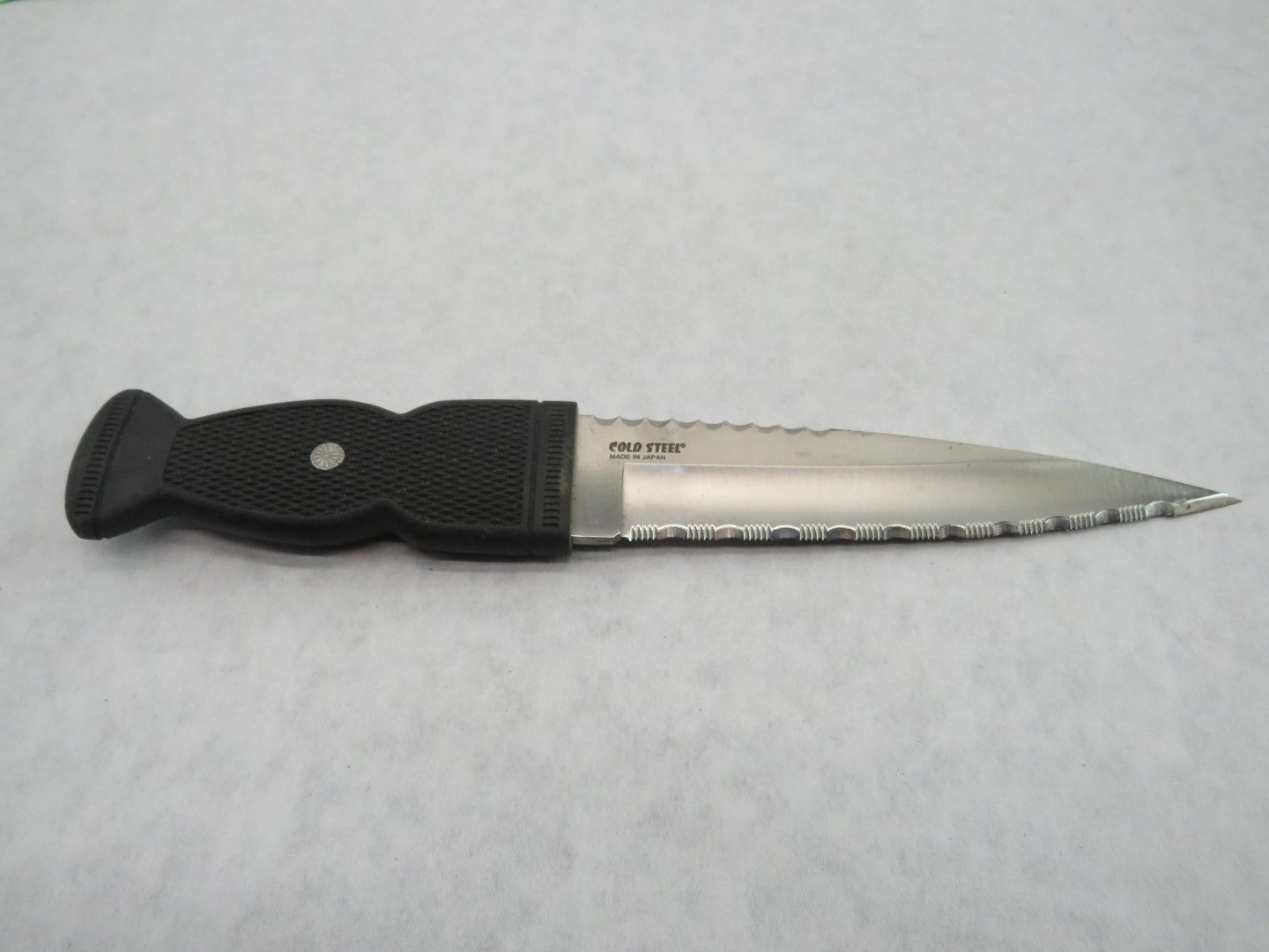 Black and silver diving knife with serrated edge on white surface.