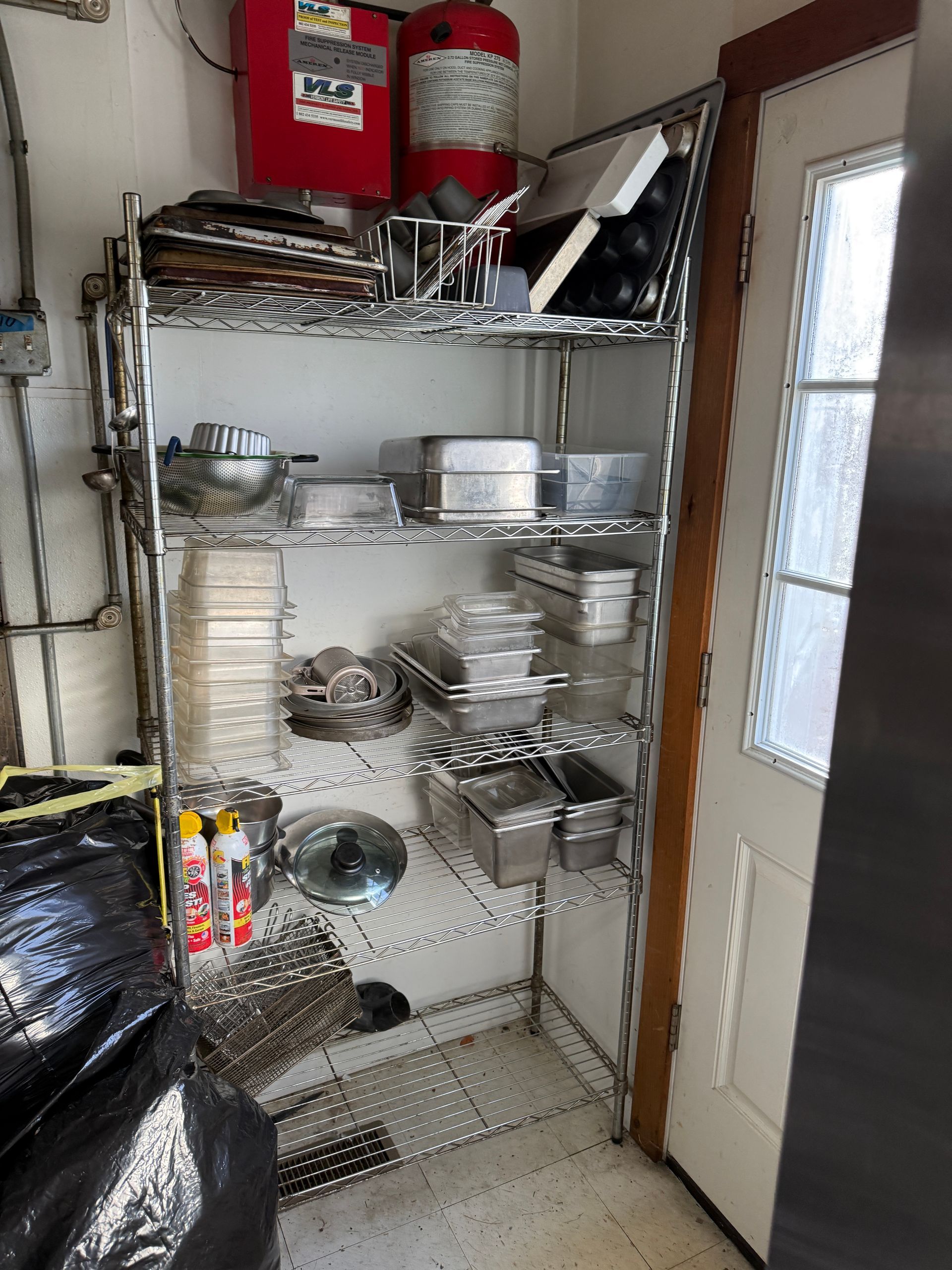 Metal shelving unit holding kitchenware next to a door, in a garage.