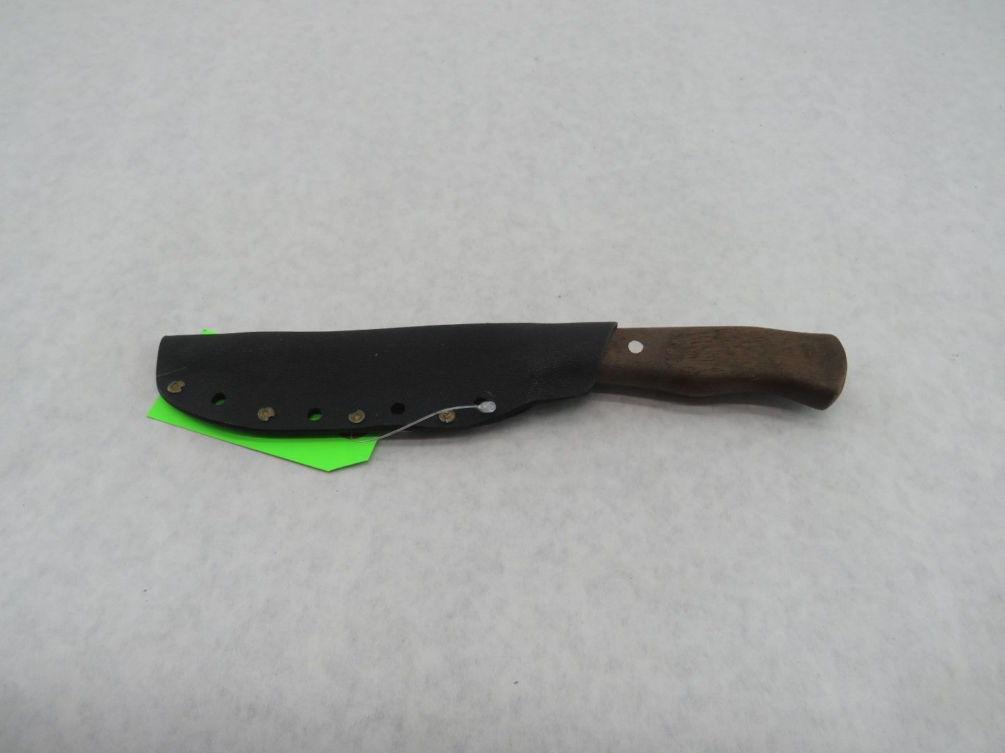Knife with wooden handle in a black leather sheath on a light surface.