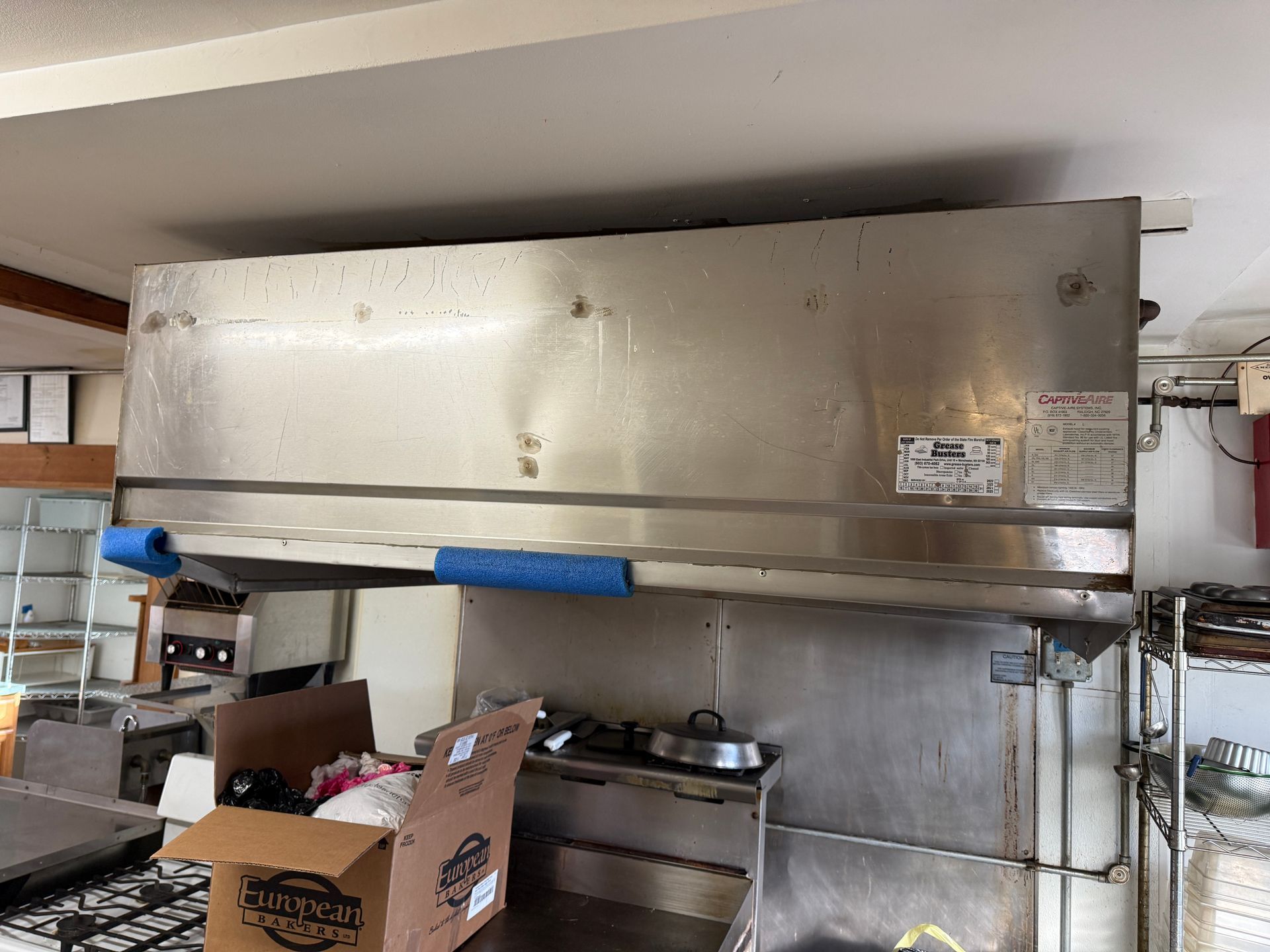 Commercial kitchen exhaust hood, stainless steel, above a countertop, blue foam padding.