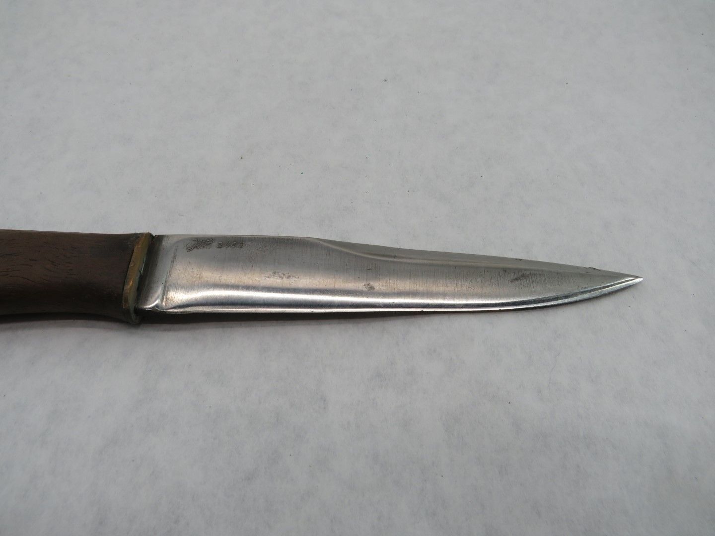 Close-up of a knife with a brown handle and a silver blade, lying horizontally on a white surface.