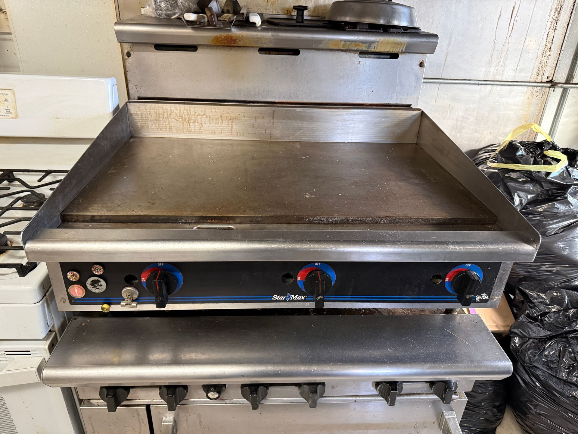 Commercial flat-top grill, stainless steel, with three control knobs and a lower shelf.