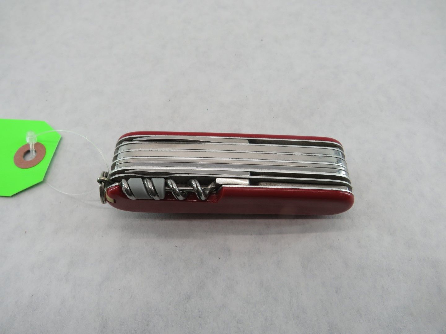 Red Swiss Army knife with multiple tools, on a gray surface with a green tag attached.