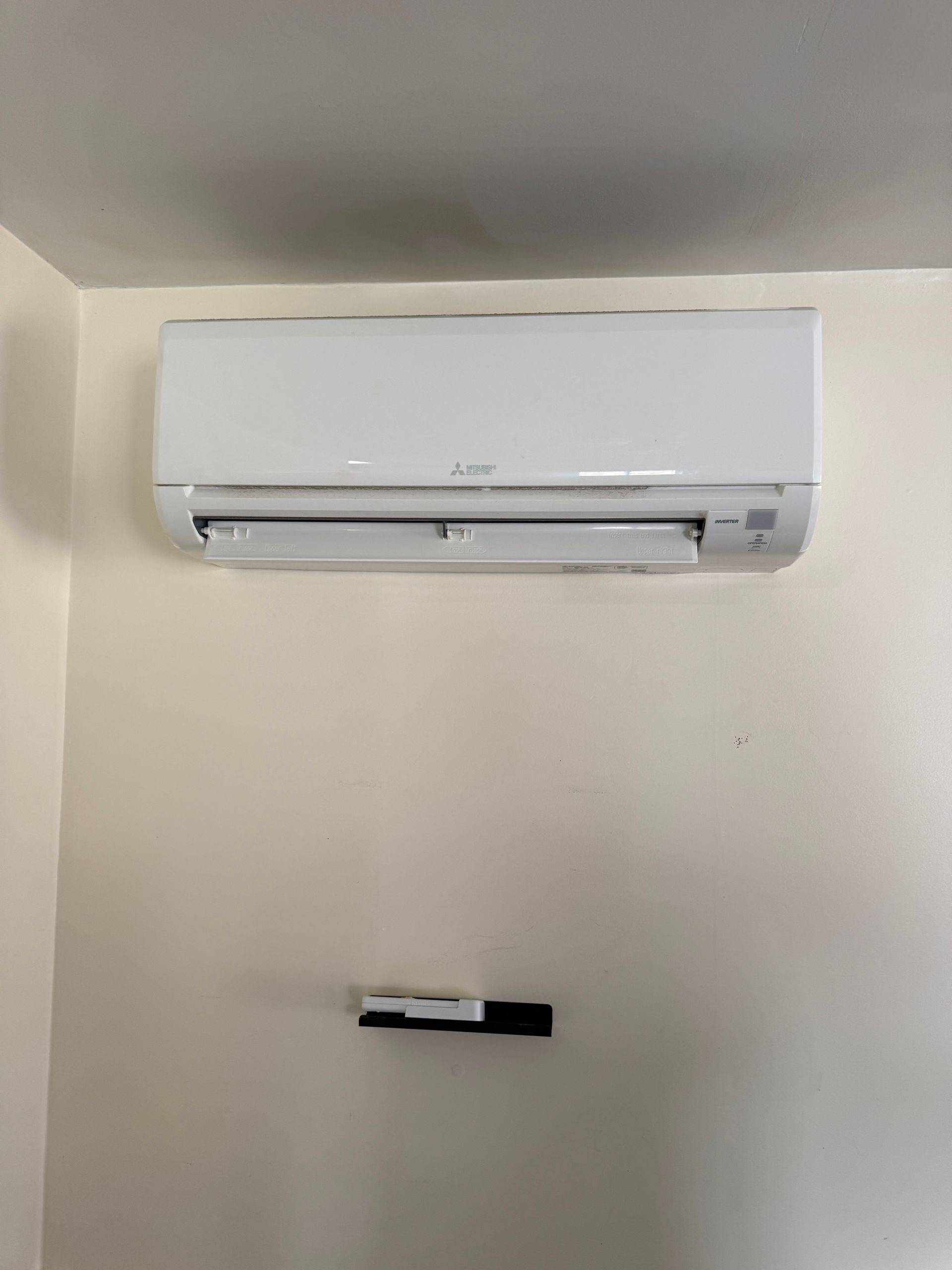 White wall-mounted Mitsubishi air conditioner above a dark bracket on a beige wall.