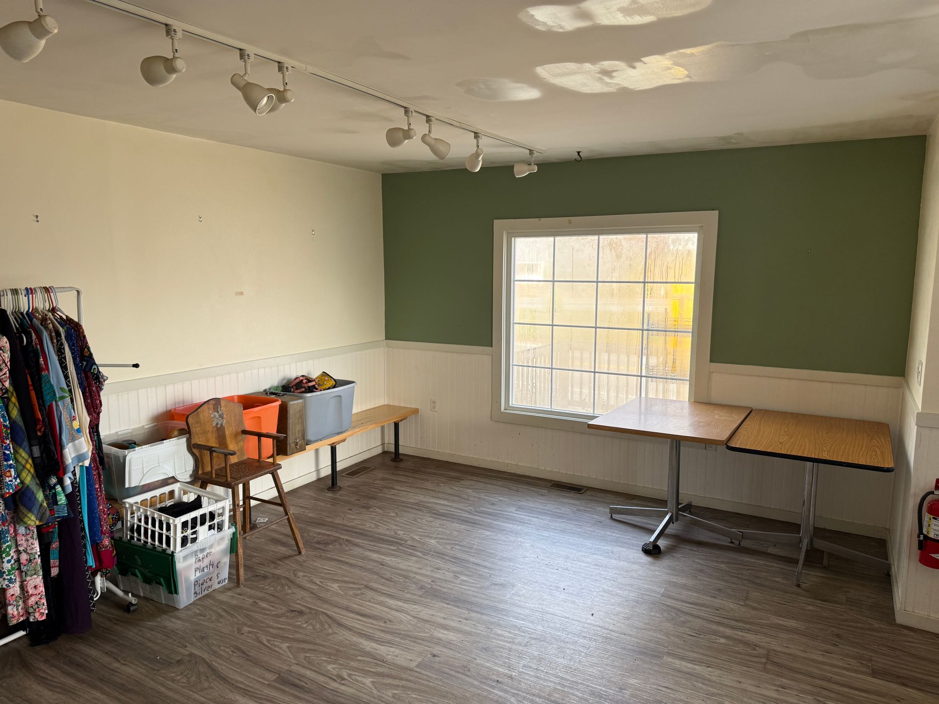 Empty room with green and white walls, wood flooring, clothes rack, window, and work table.