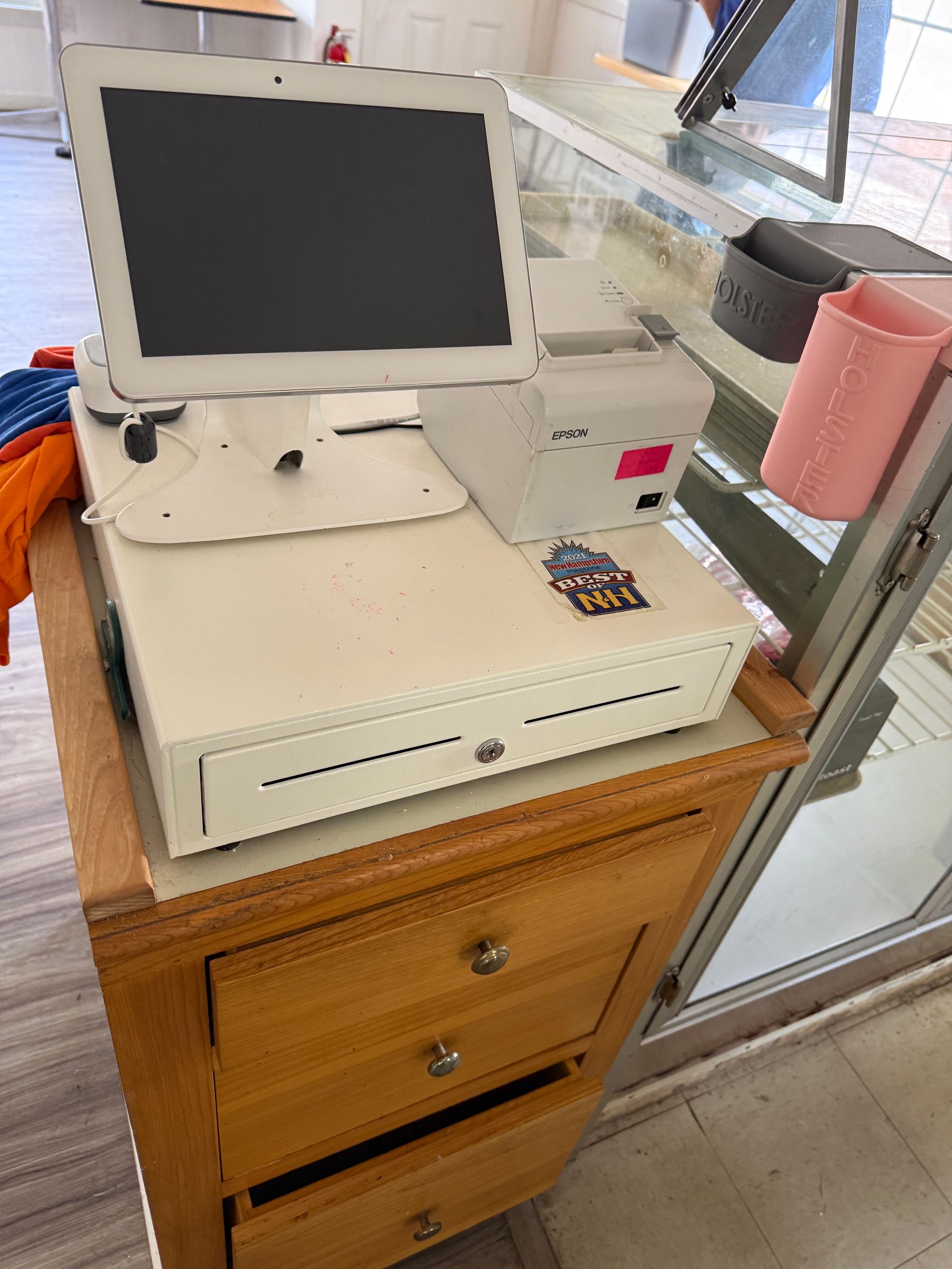 Cash register with monitor and printer on a wooden cabinet.