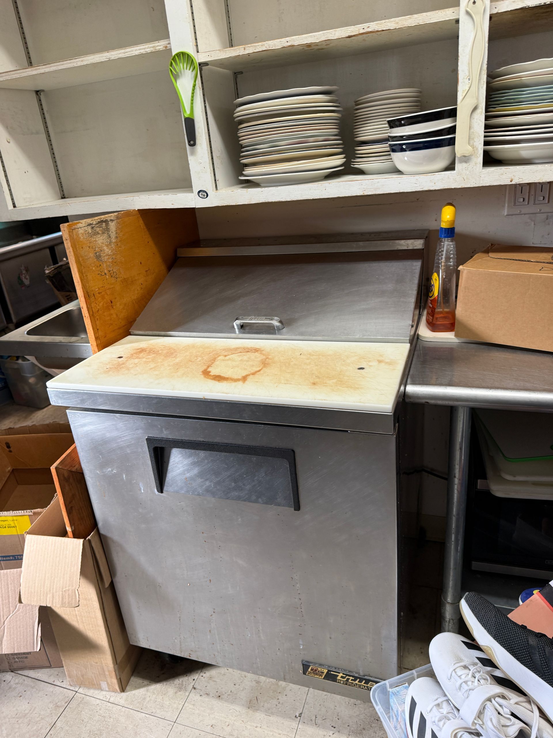 Stainless steel kitchen refrigerator with open lid, near shelves with dishes.