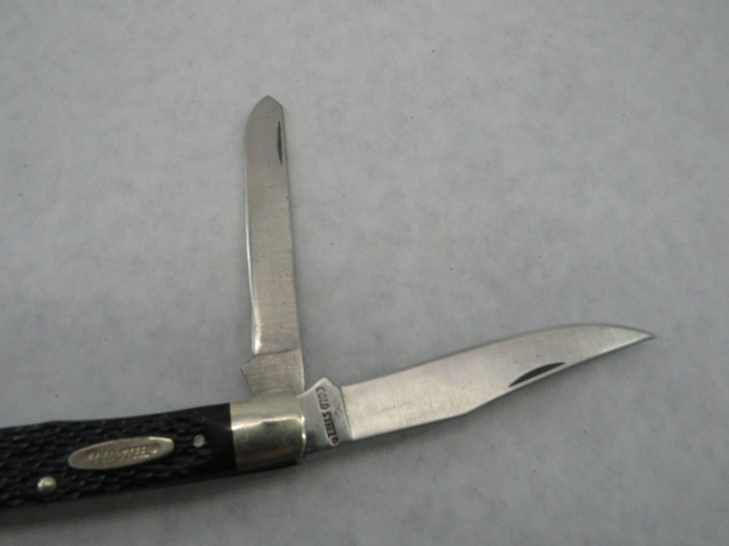 Pocket knife with two open blades, black handle, gray background.