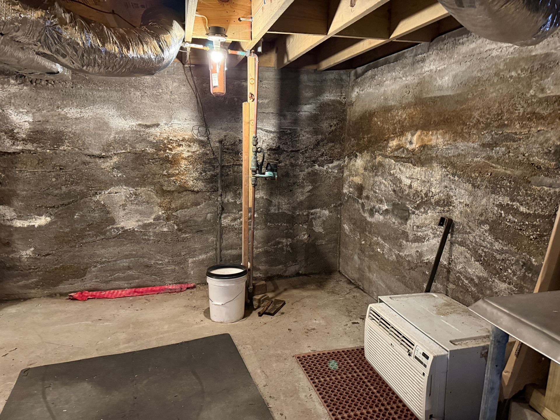 Basement with concrete walls, a bucket, and an air conditioner.