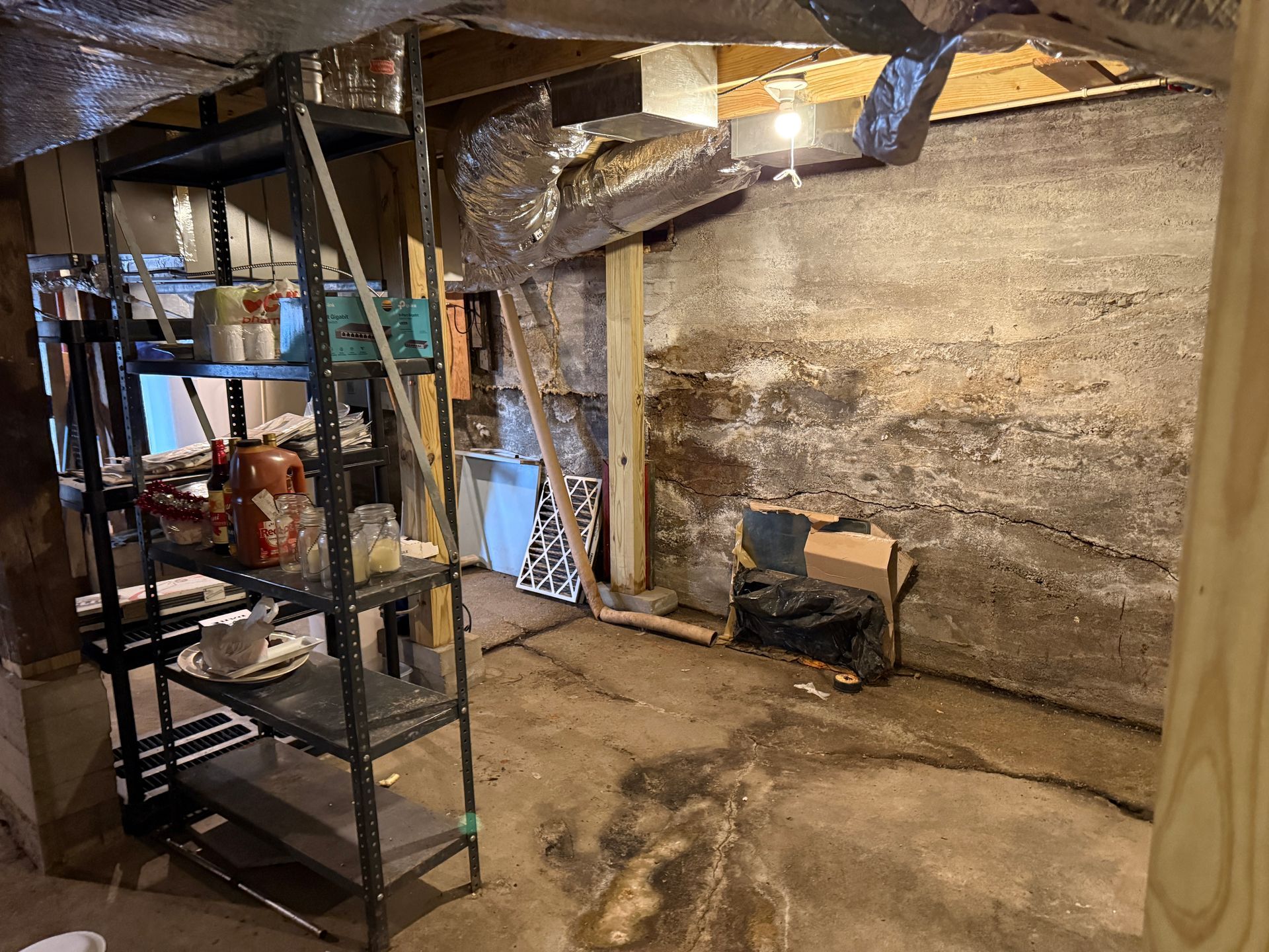 A basement interior with shelving, concrete walls, and ductwork.