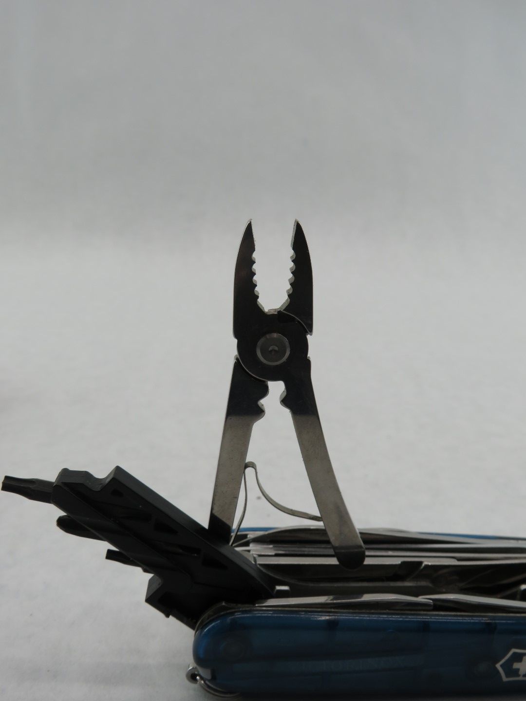 Multi-tool with pliers extended. Blue handle with black tools. Bright background.