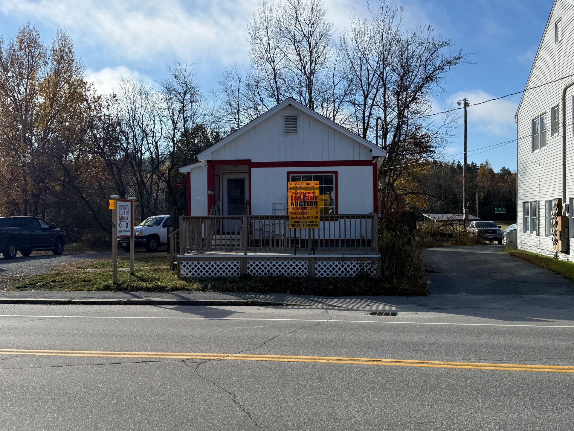 Small white building with red trim and a porch, roadside, with a sign in front.