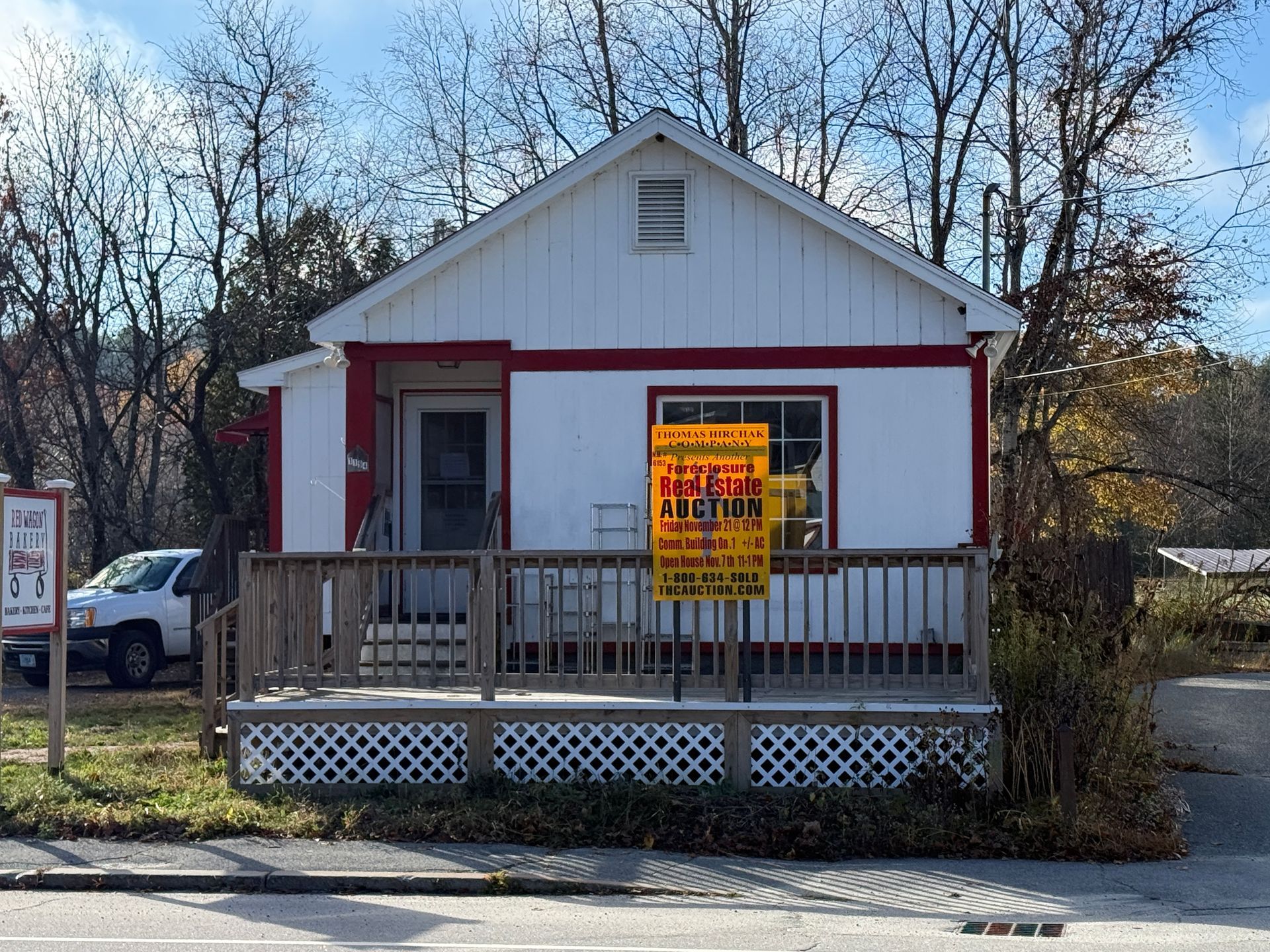 Small white building with red trim, porch, and a 