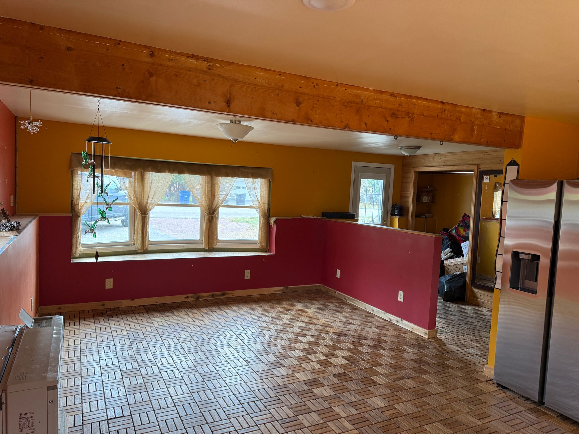 Kitchen with red and yellow walls, wooden beam, and large stainless steel refrigerator.