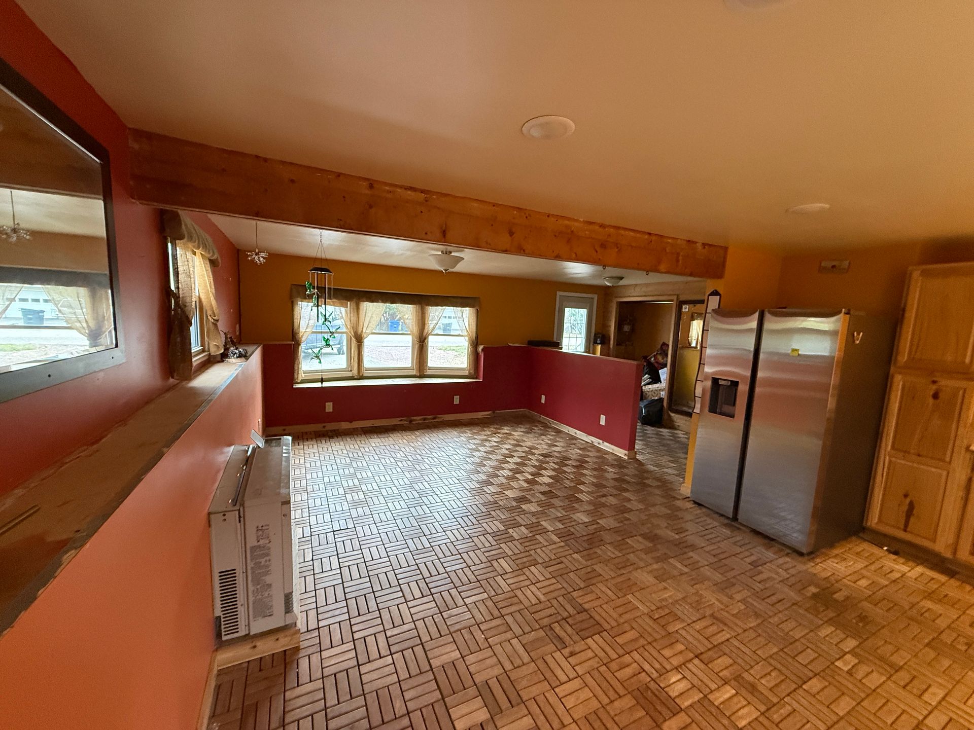 Open-concept kitchen with wood block flooring, exposed beam, red and yellow walls, stainless steel refrigerator.