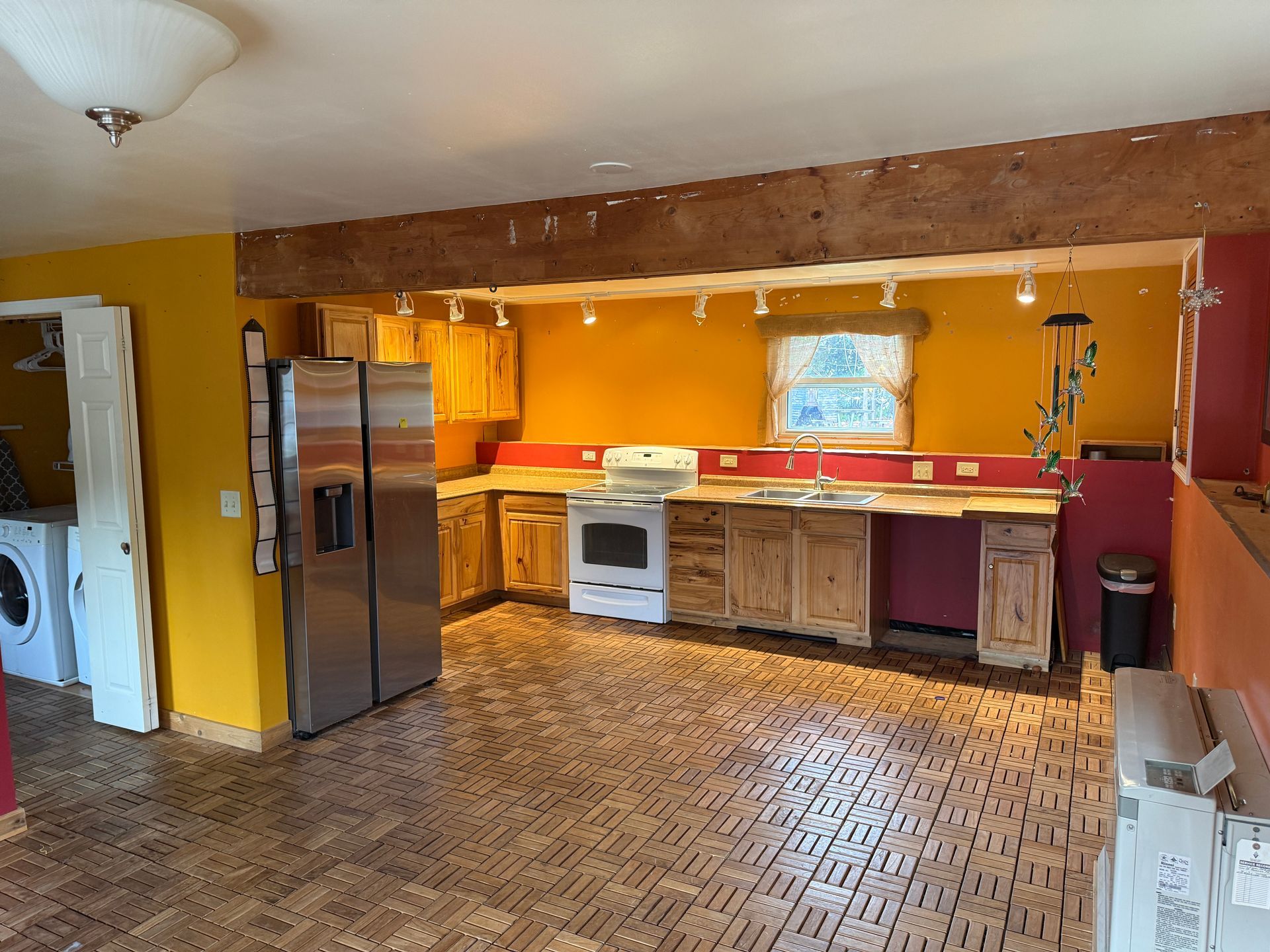 Kitchen with wood cabinets, stainless steel refrigerator, yellow and red walls, and wood floor.