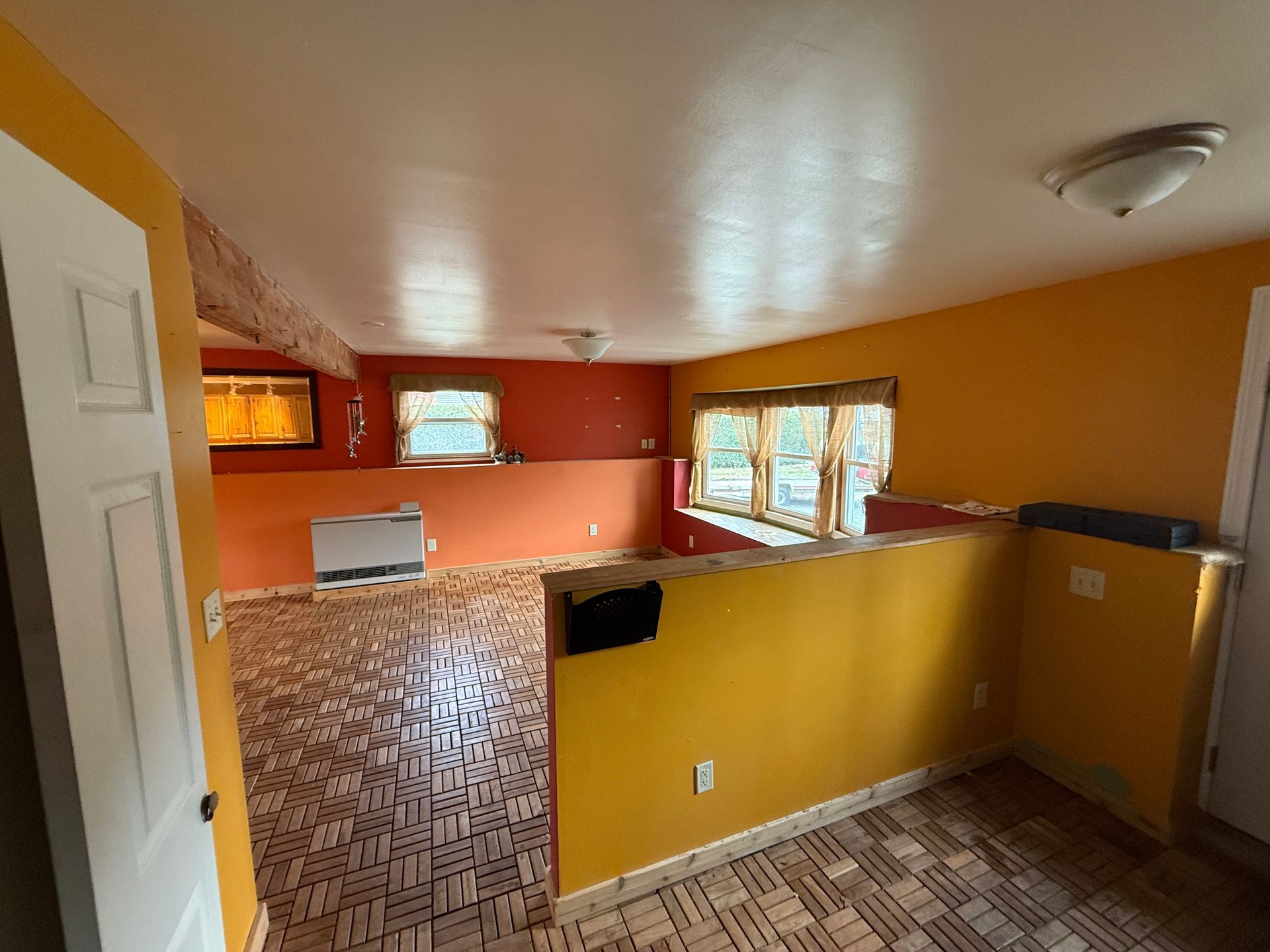 Interior of a room with orange walls, wood floor, and two windows. One white door is open.
