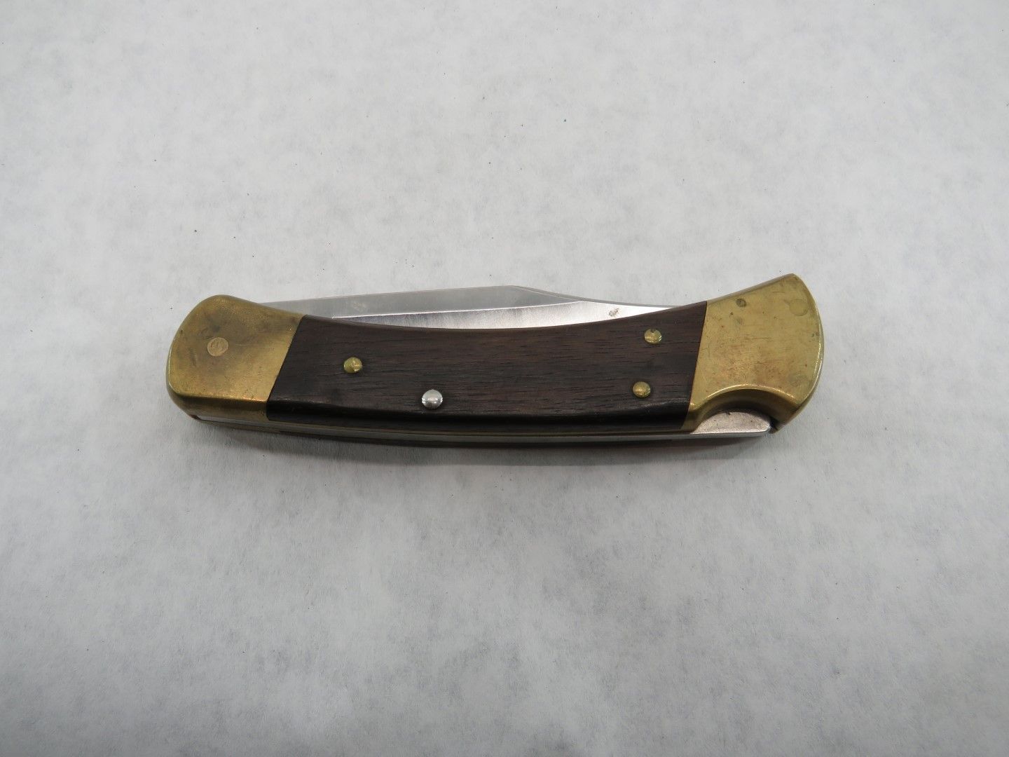Closed pocket knife with brass bolsters and dark wooden handle.